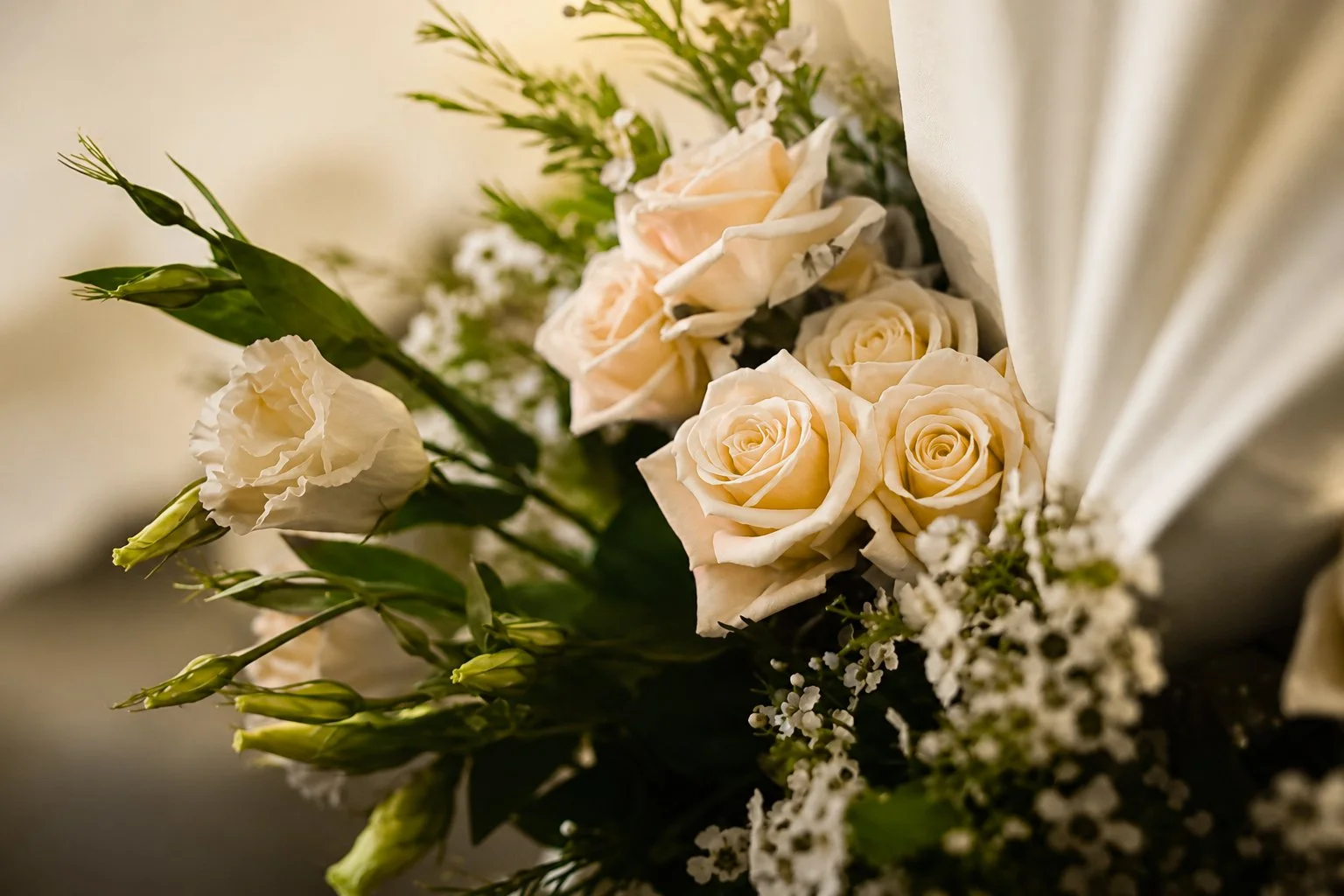A bouquet of light peach and white roses along with small white flowers and green foliage.