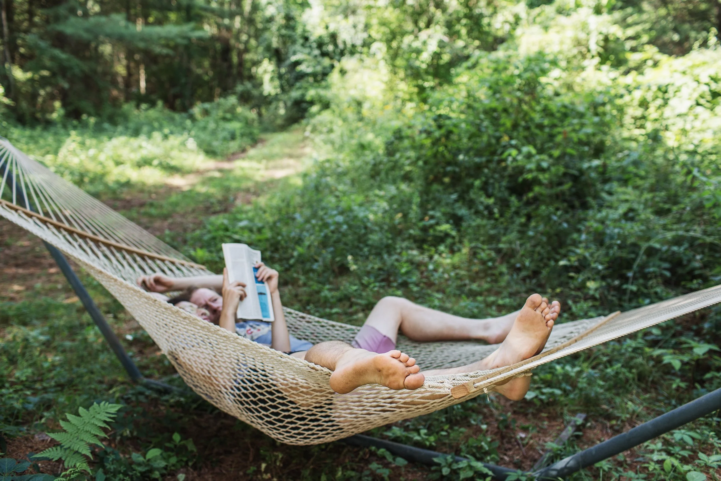 Person lying in a hammock reading a book in a lush, green forest.