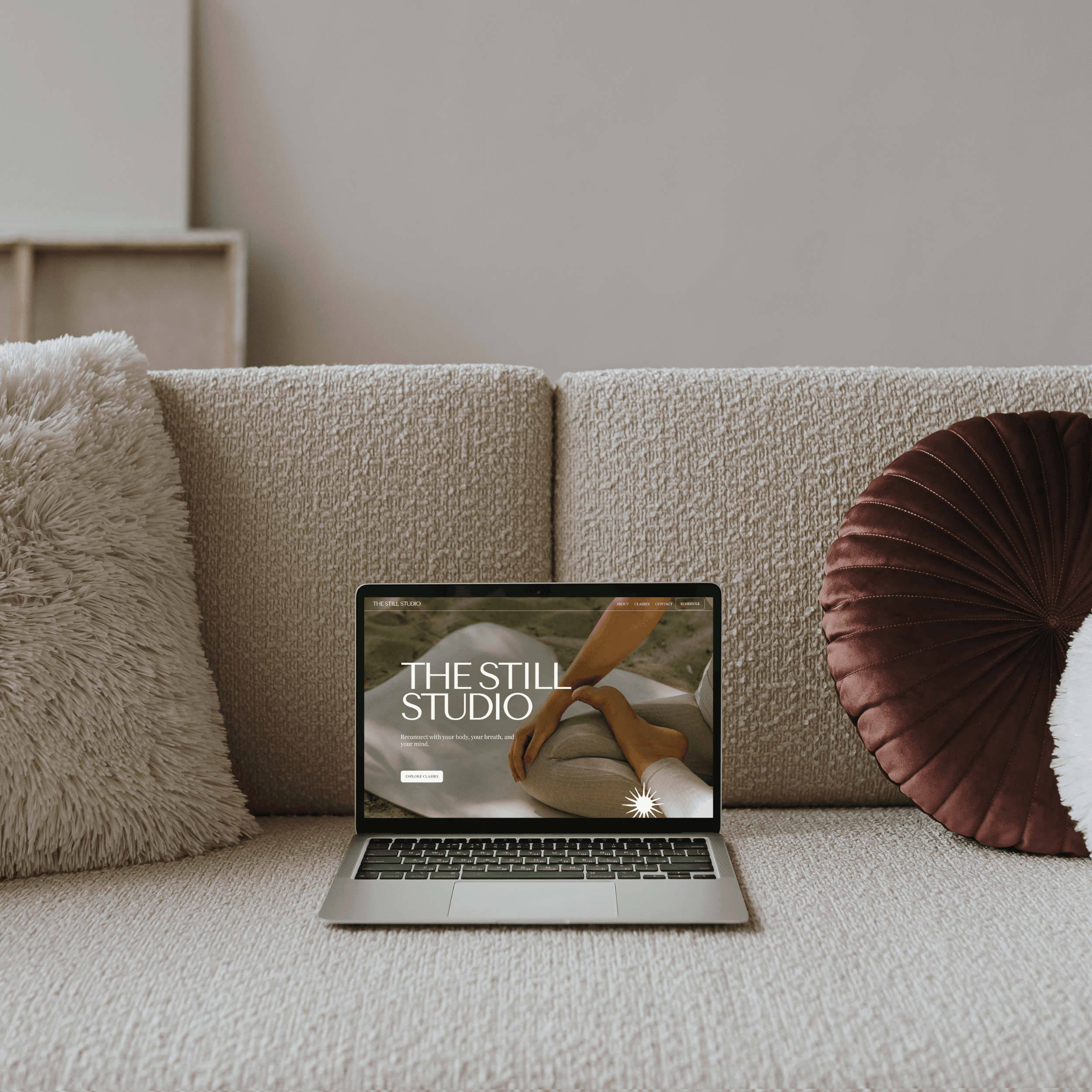 A luxury cream sofa with an open laptop sitting on it showing the home page of a luxury beach yoga studio.