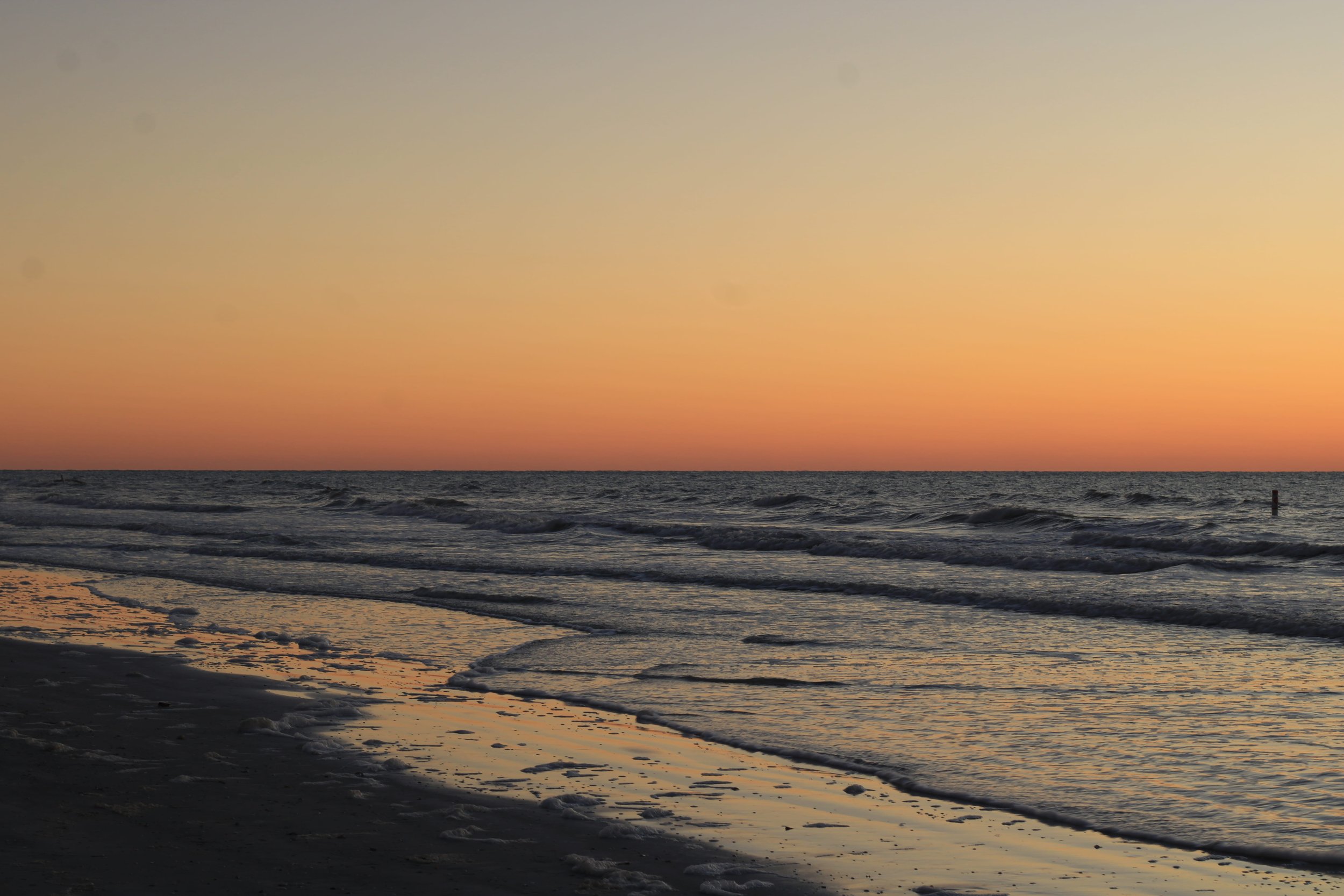 A beautiful sunset with a clear bright sky and reflections playing off of the shore and water coming in.