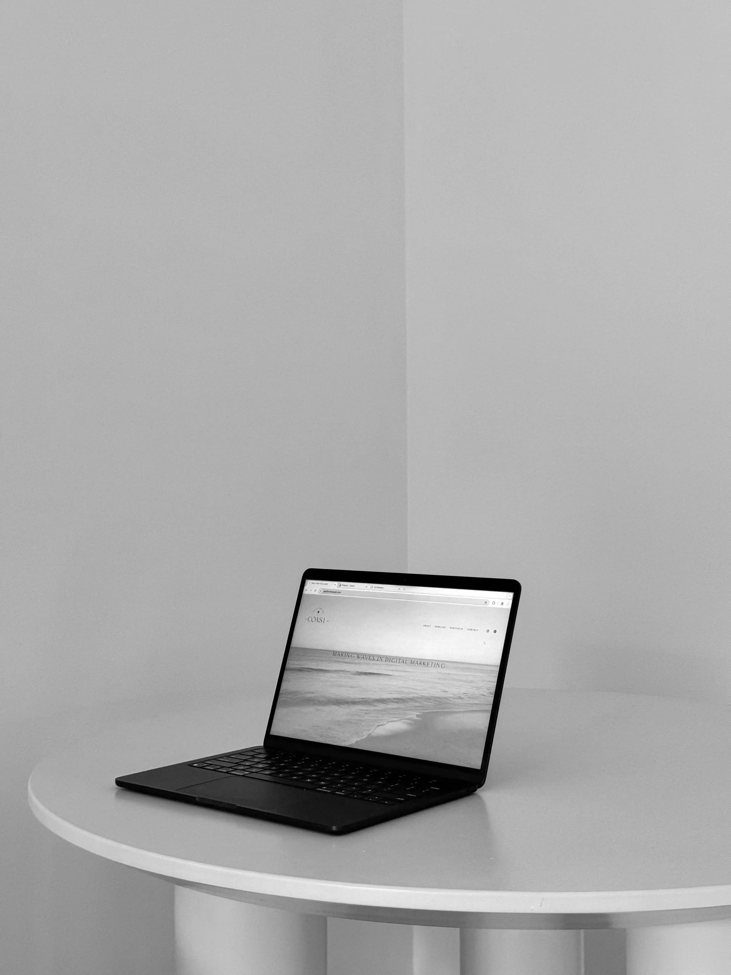 Minimal and modern workspace with just a round table and a laptop showing a beach sunrise background.