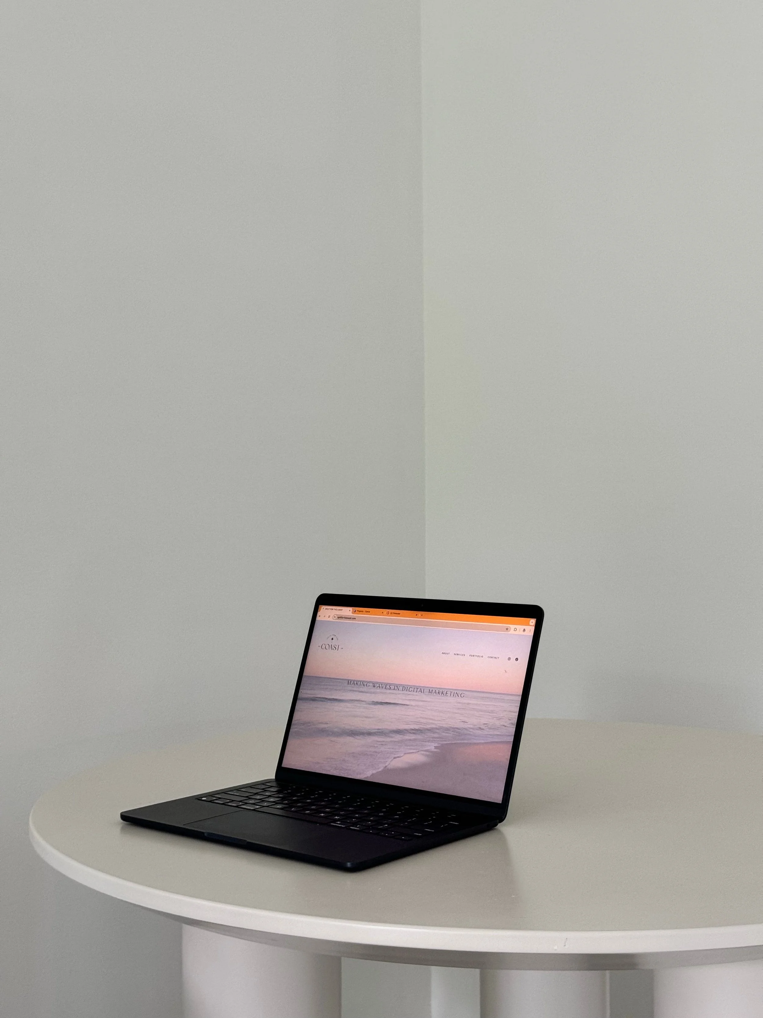 Minimal and modern workspace with just a round table and a laptop showing a beach sunrise background.