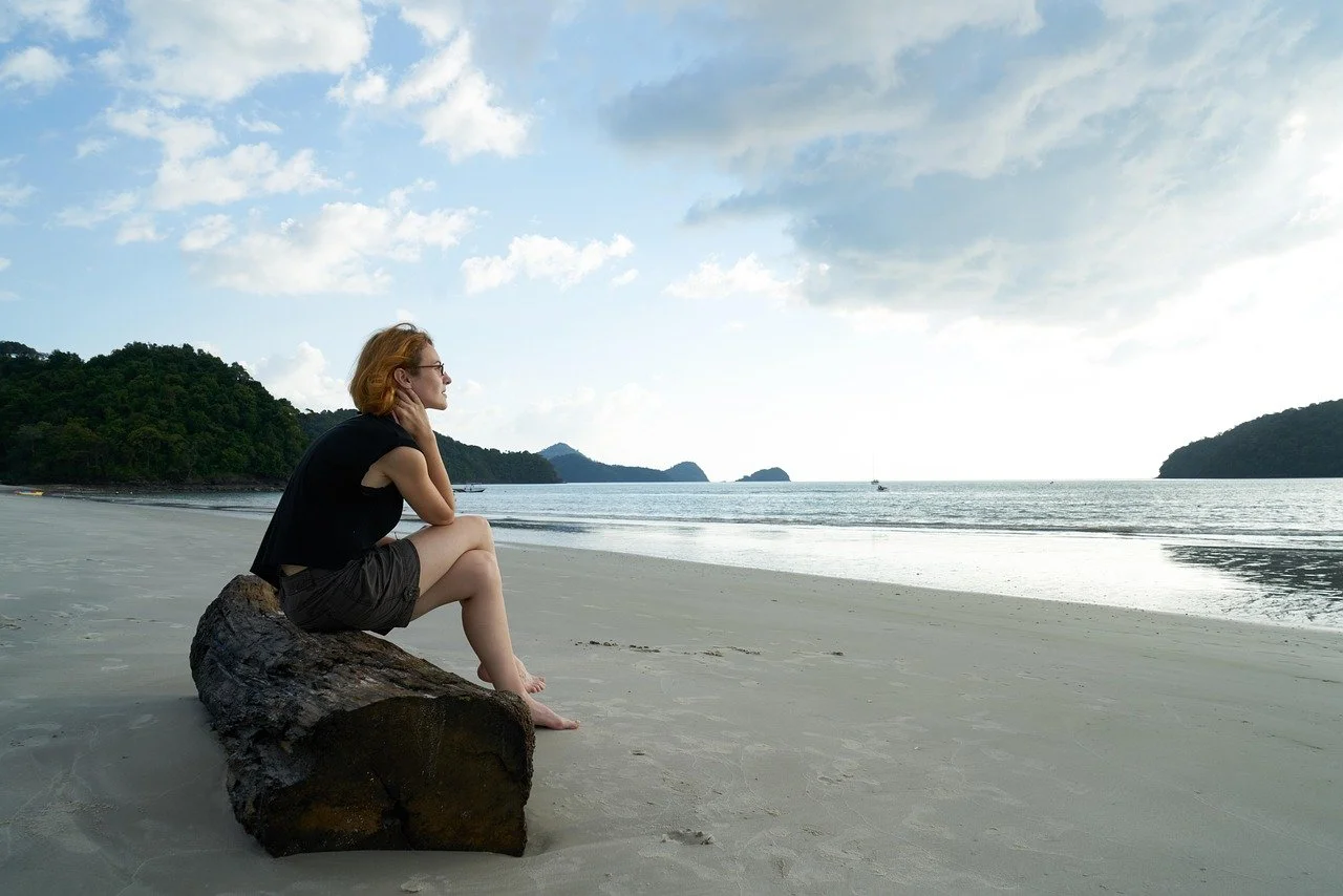 A woman sitting on a log while thinking. Is trauma from the past affecting your parenting style in the present? Online therapy for mothers in Mill Creek, WA, can help you heal from past trauma and strengthen your role as a mother.