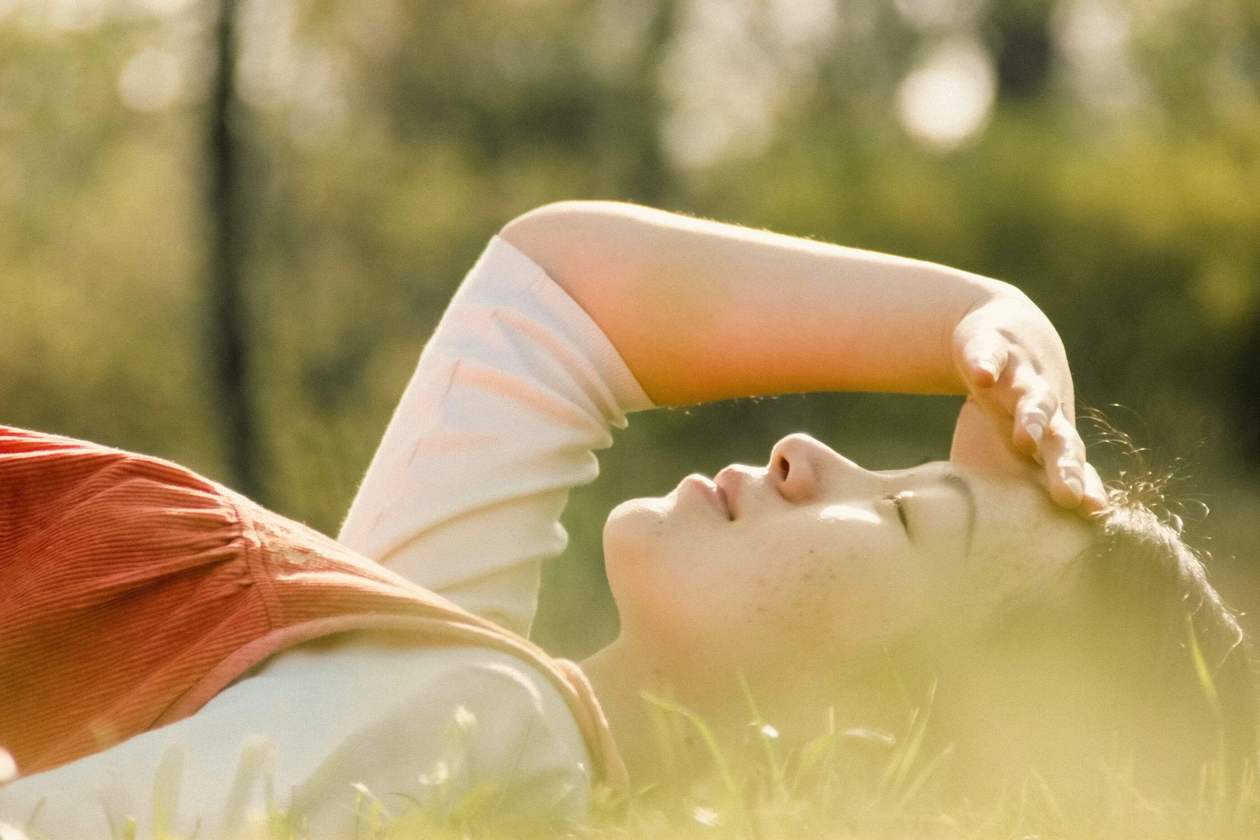 A woman lies peacefully in the grass with her eyes closed, resting in warm sunlight. How can healing help the body move from constant vigilance toward calm and regulation? Trauma therapy in Mill Creek, WA, offers compassionate support for recovery.