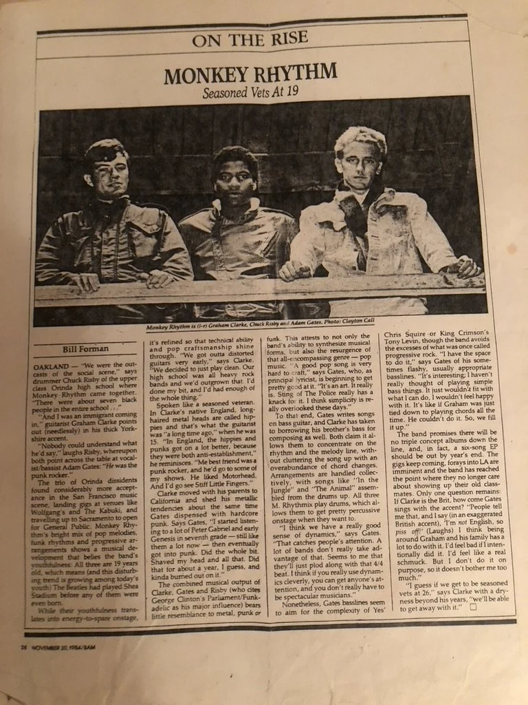 Black and white photo of three young men sitting at a table, with a newspaper headline above them that reads 'Monkey Rhythm' and subheading 'Seasoned Vets at 19.'