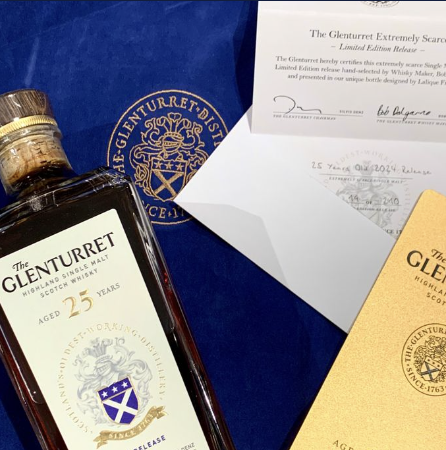 A bottle of The Glenturret 25 Year Old Highland Single Malt Whisky, a certificate, and a yellow booklet display on a blue surface.
