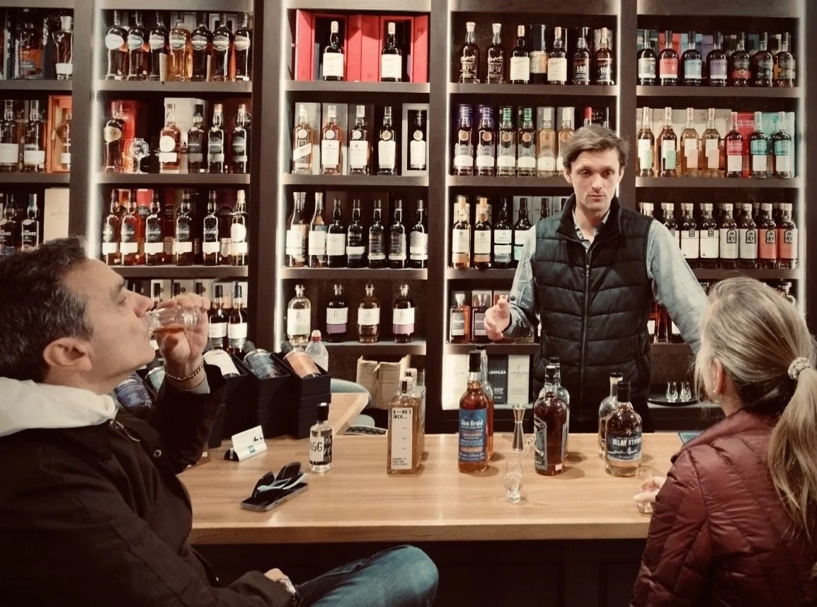 Man conducting a whiskey tasting session with two participants in a store filled with shelves of whiskey bottles.