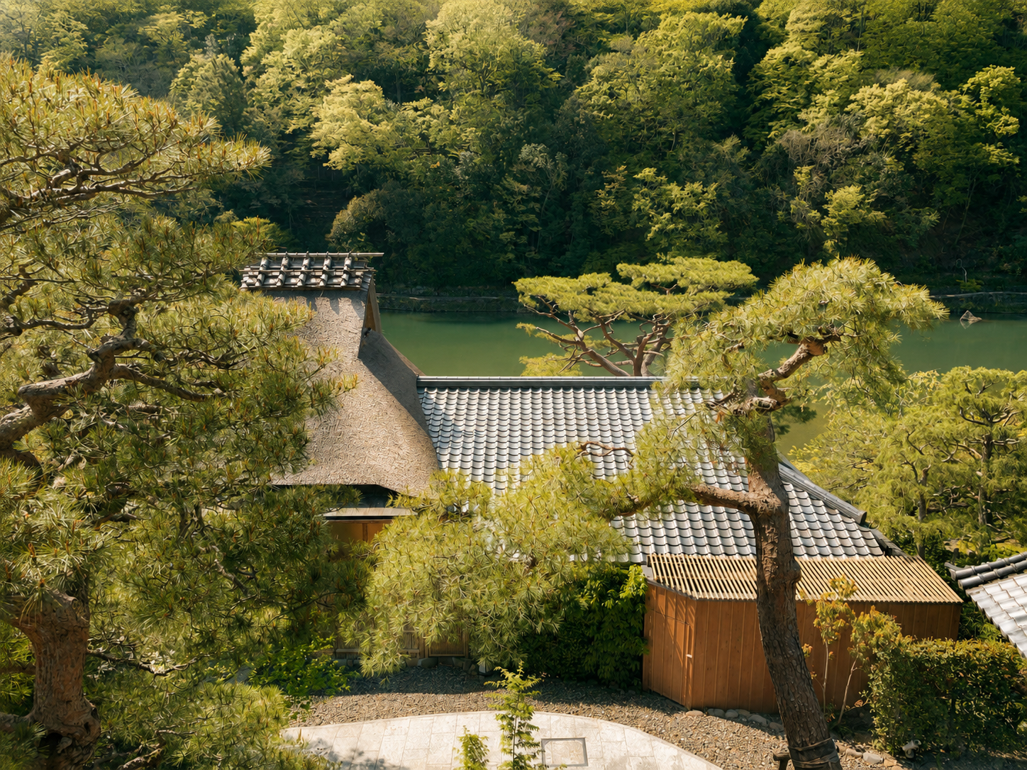 Vista aérea de la arquitectura tradicional con techo de paja de Café Hassui en Suiran, a Luxury Collection Hotel, Kyoto, rodeado de pinos y frente a las aguas verdes del río Hozu en Arashiyama.