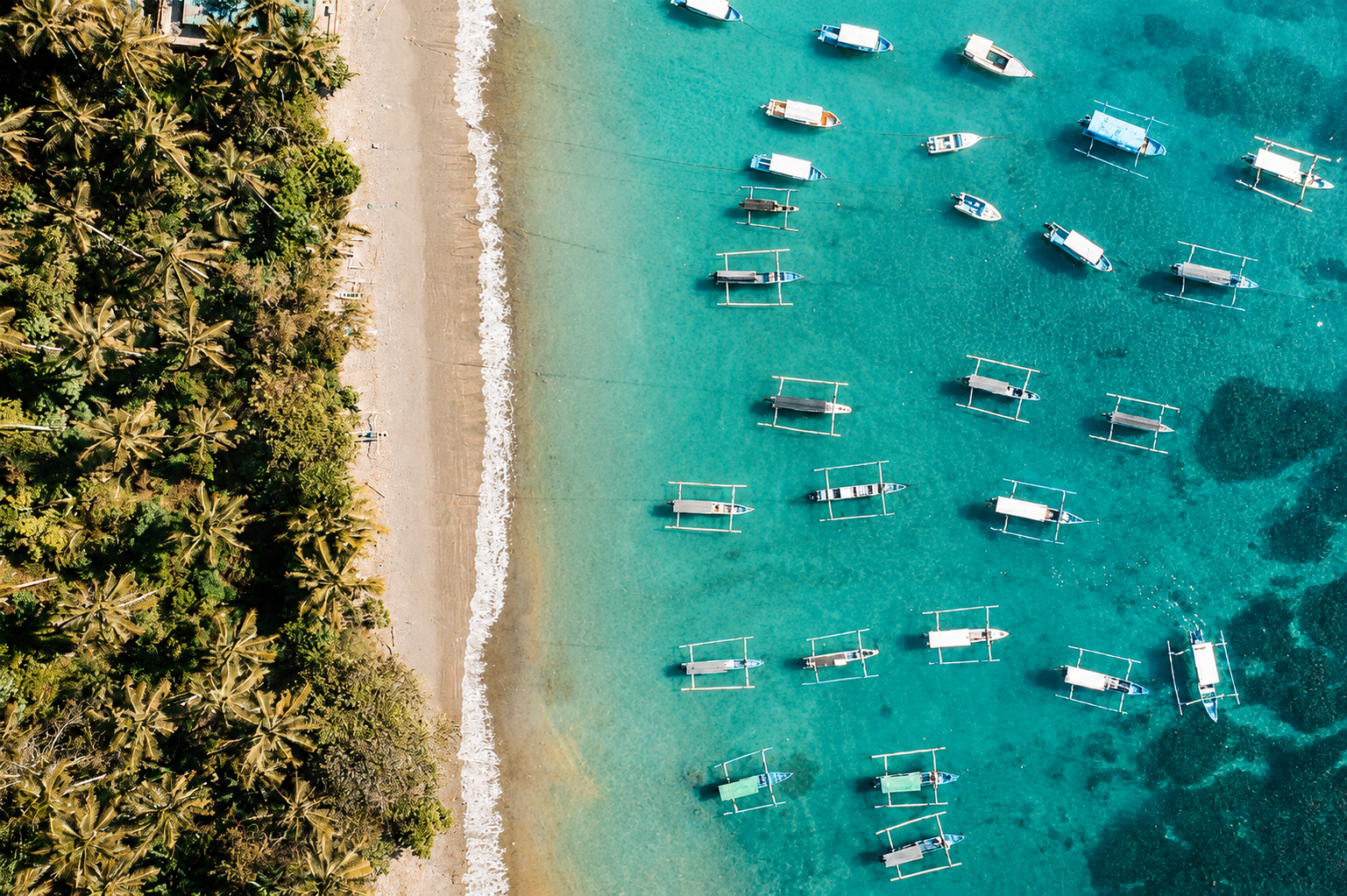 Vista aérea con dron de barcos tradicionales jukung flotando en las aguas turquesas de Candidasa, representando el ecoturismo y la costa del este de Bali.