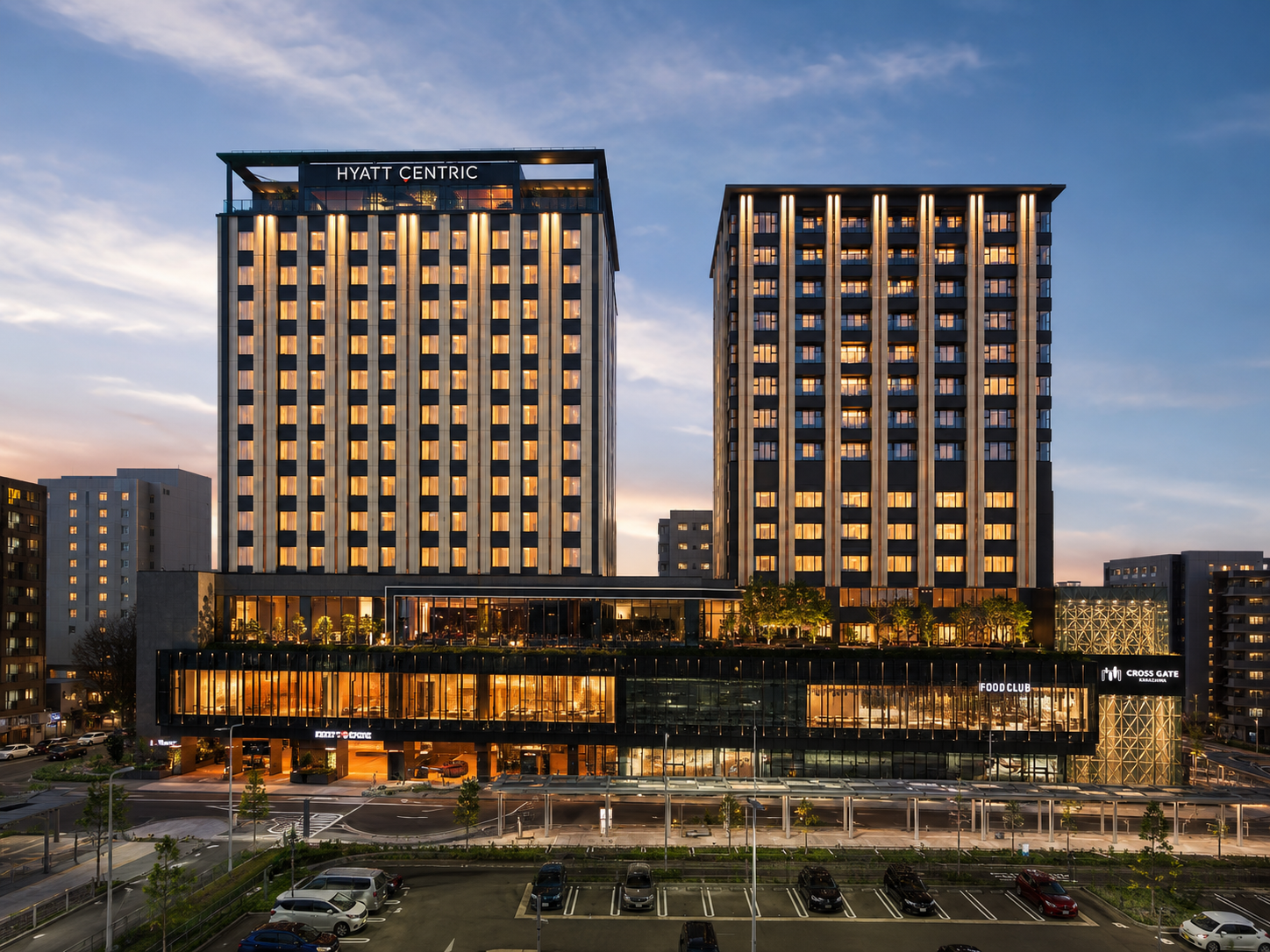 Fachada exterior moderna de los dos edificios del hotel de lujo Hyatt Centric Kanazawa e instalaciones de Cross Gate Kanazawa completamente iluminadas durante el atardecer.