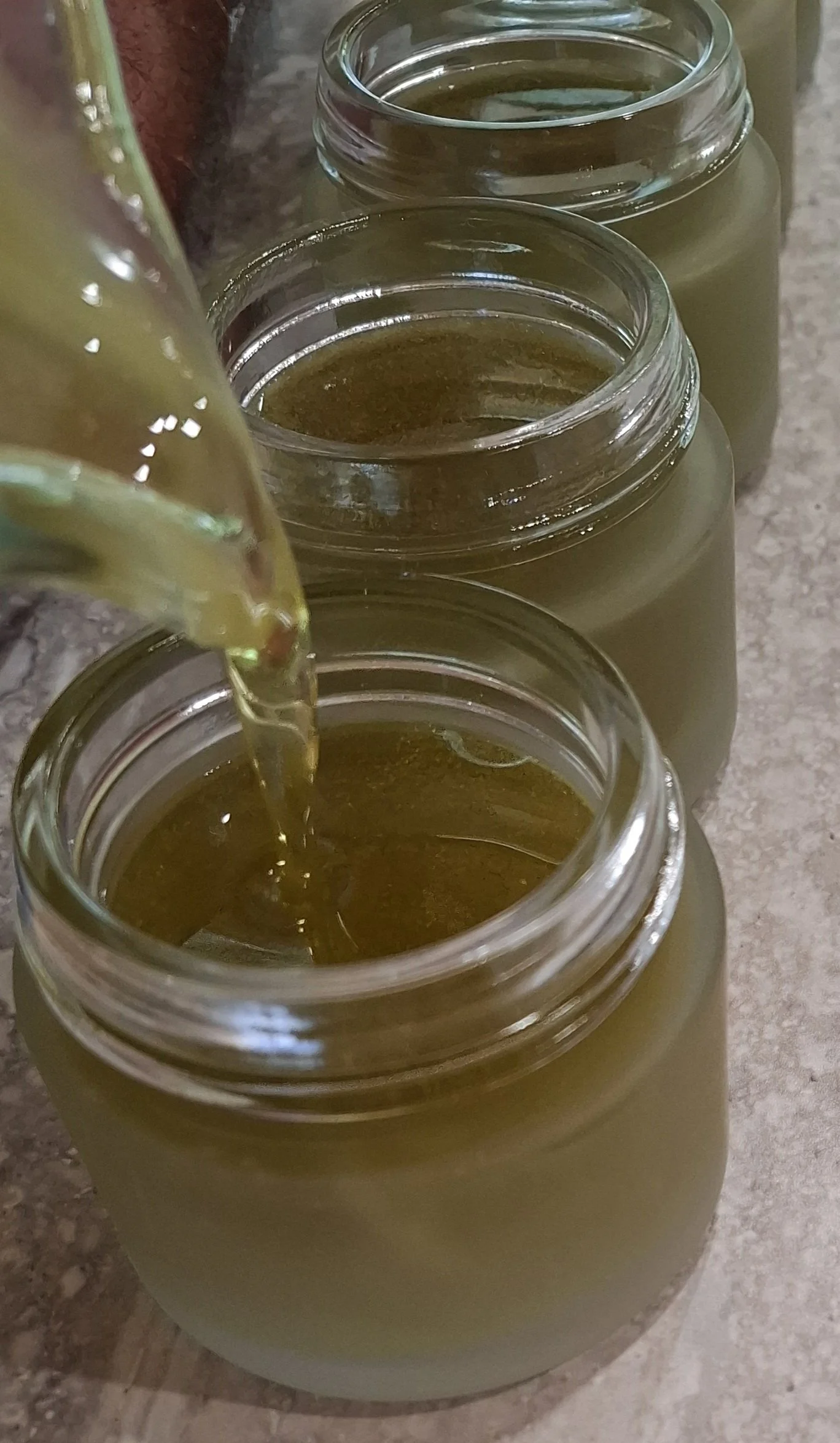 Multiple glass jars filled with a yellowish-green liquid, with one jar being poured into from a bottle.
