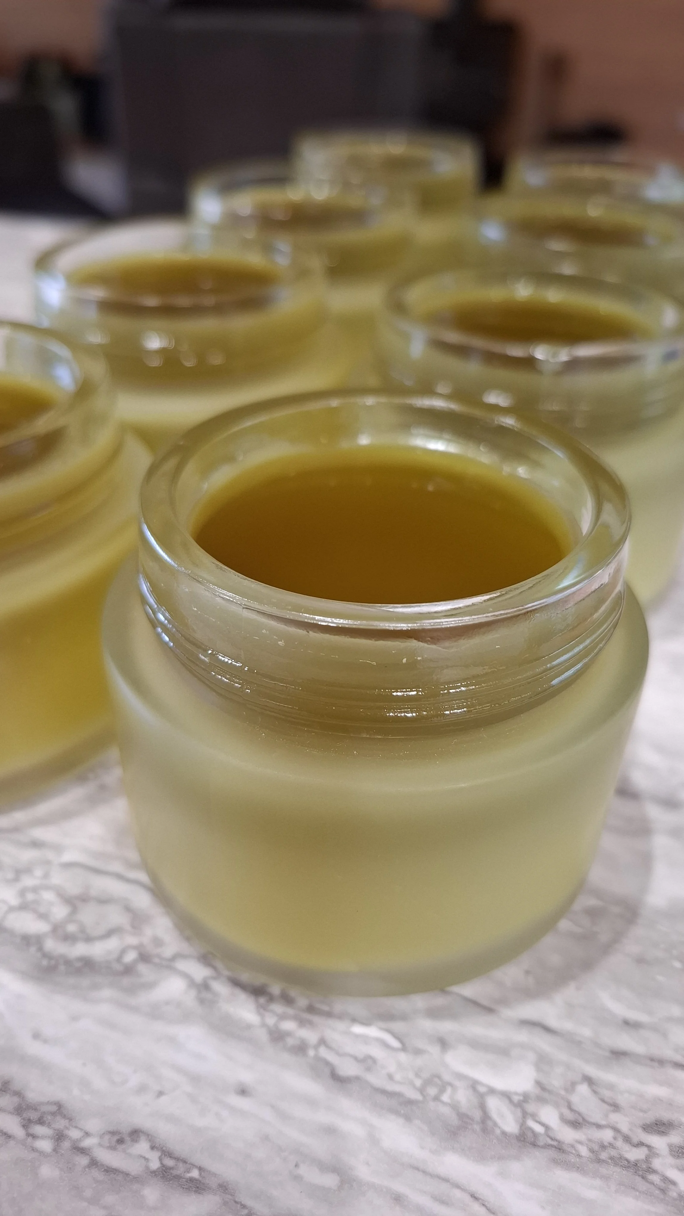 Several small glass jars filled with a yellowish, translucent liquid, arranged on a speckled gray surface.
