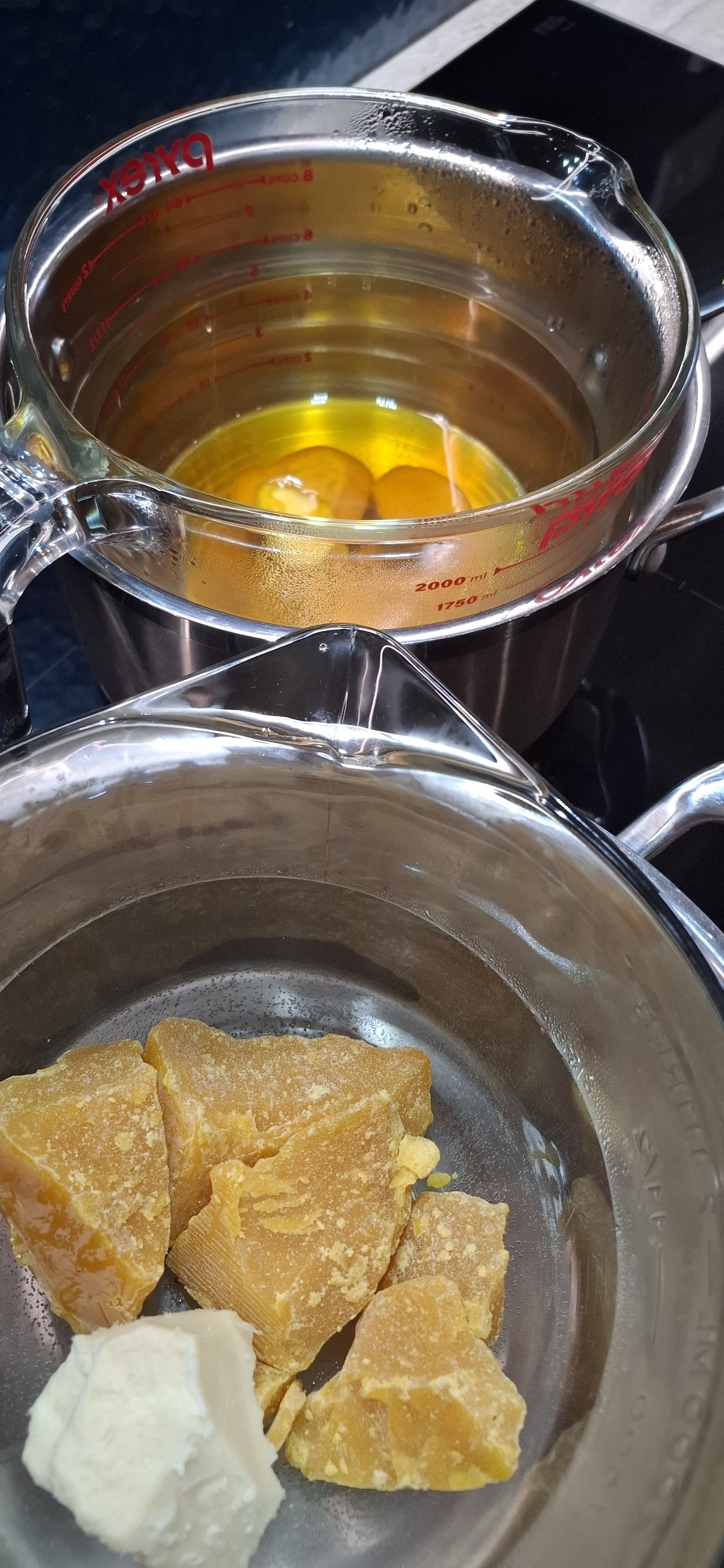 A silver mixing bowl with pieces of yellow and white. Behind it, there is a glass measuring cup with condensation and small bubbles visible.