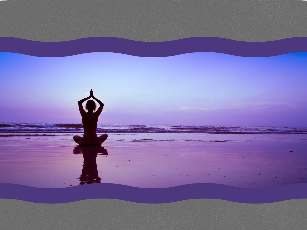 Silhouette of a person practicing yoga on the beach during sunset, with their hands in a prayer position above their head, reflected in the wet sand.