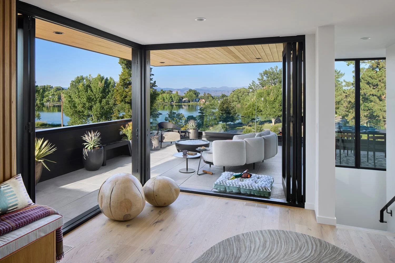 Modern living room opening to a balcony with lake and trees scenic view