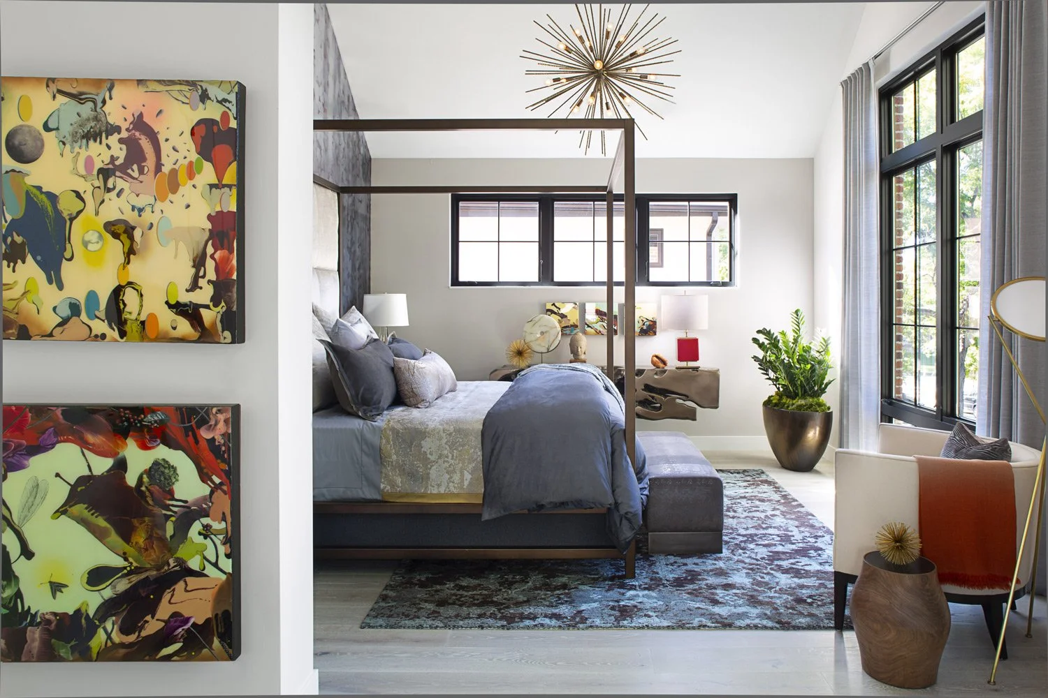 Modern bedroom with dark wood four-poster bed, abstract artwork on the wall, and large windows with gray curtains, decorated with a large plant, colorful rug, and contemporary furniture.