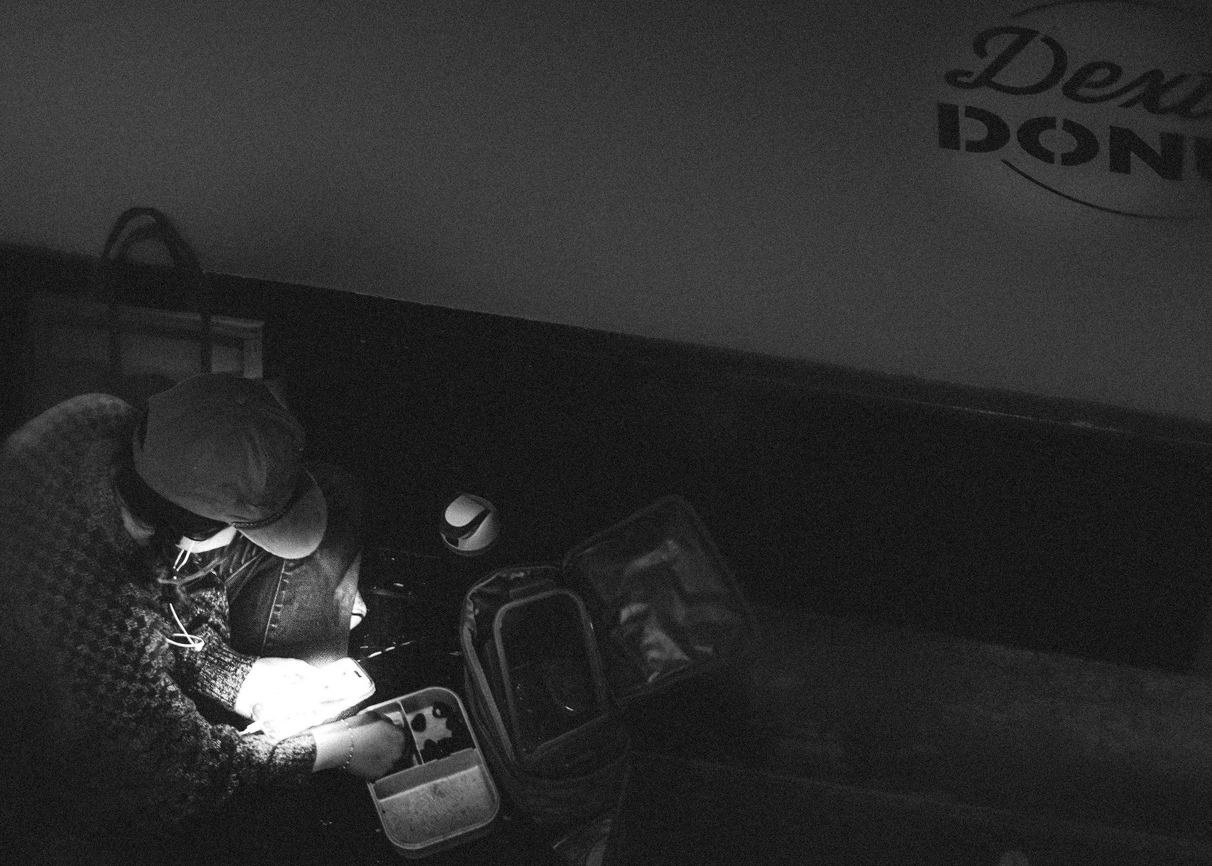 A black and white image of a cluttered workspace with various containers, a notebook, and miscellaneous items scattered around.