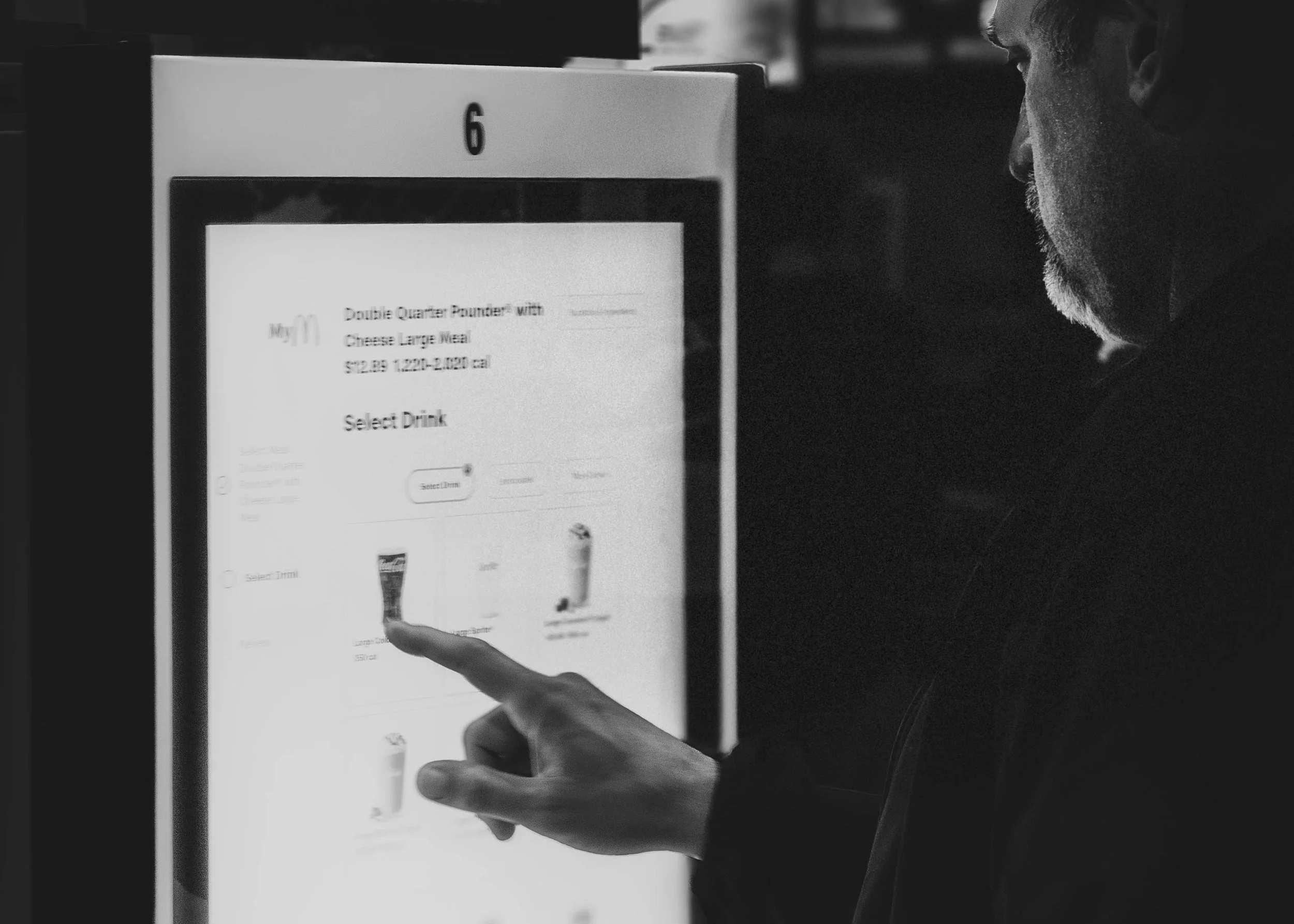 Black and white image of a person with a beard pointing at a touchscreen menu, which mentions a double quarter pounder with cheese and a large meal.