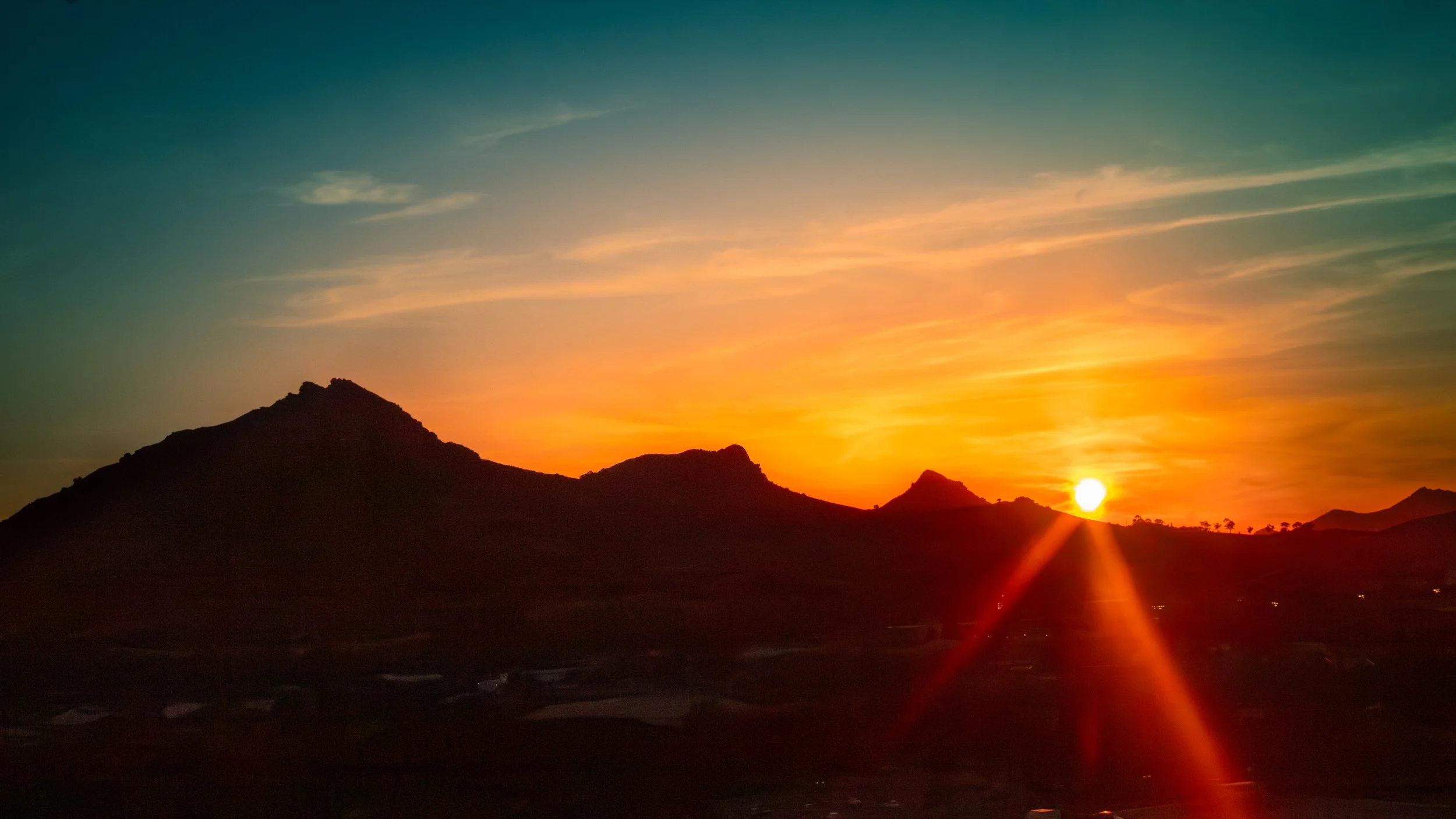 Sunset over a mountain range with colorful sky and silhouette of hills.