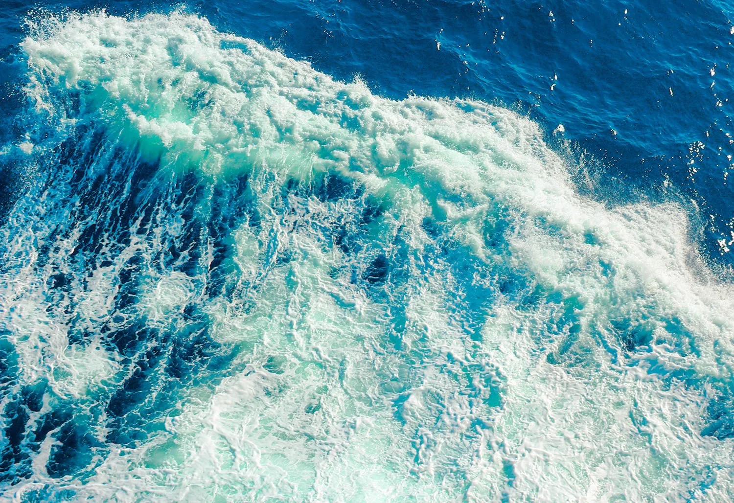 Choppy blue ocean water with white foam from a moving boat