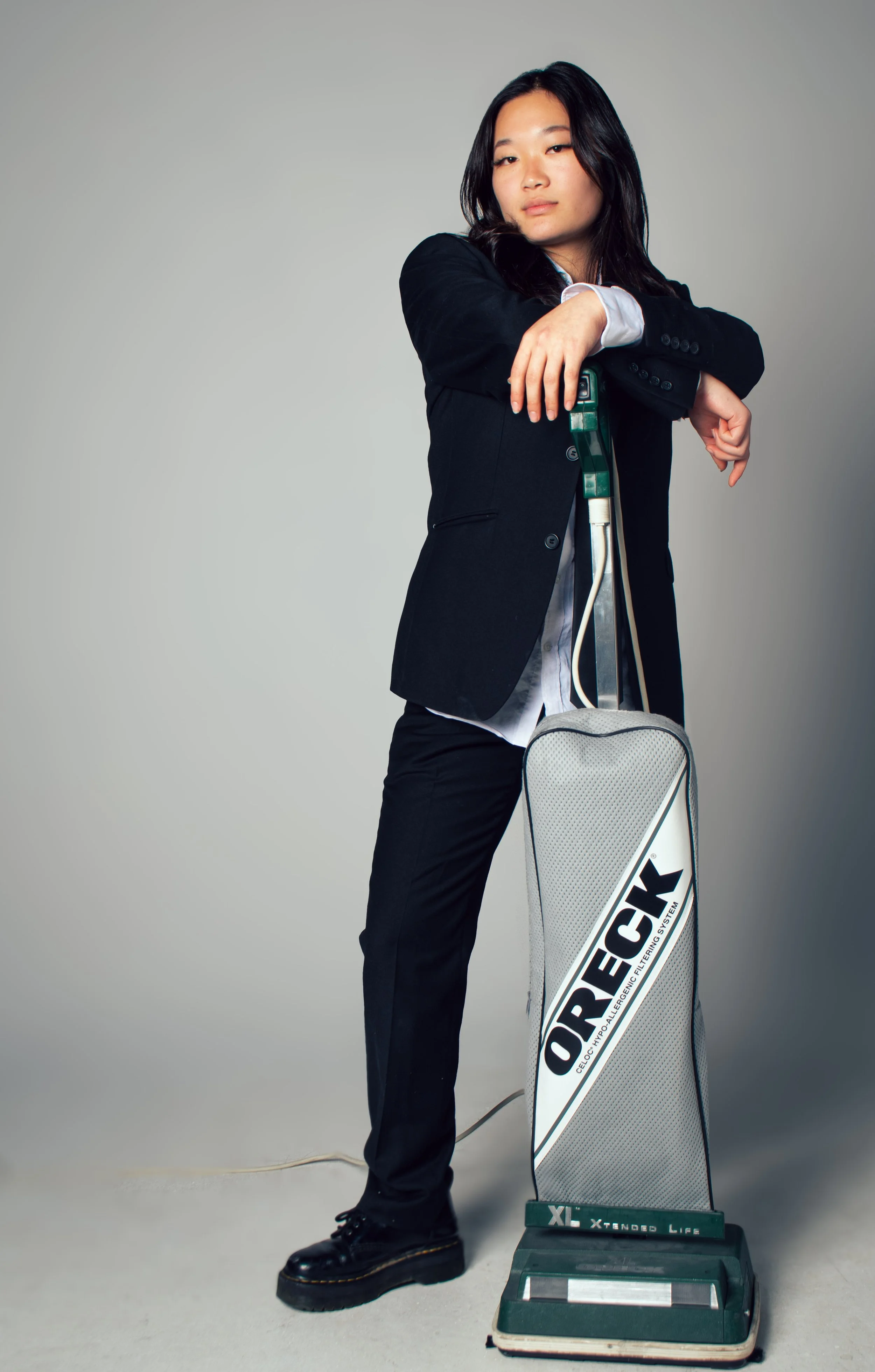 Young woman in black suit posing with crutches and a standing support device in front of a gray background.