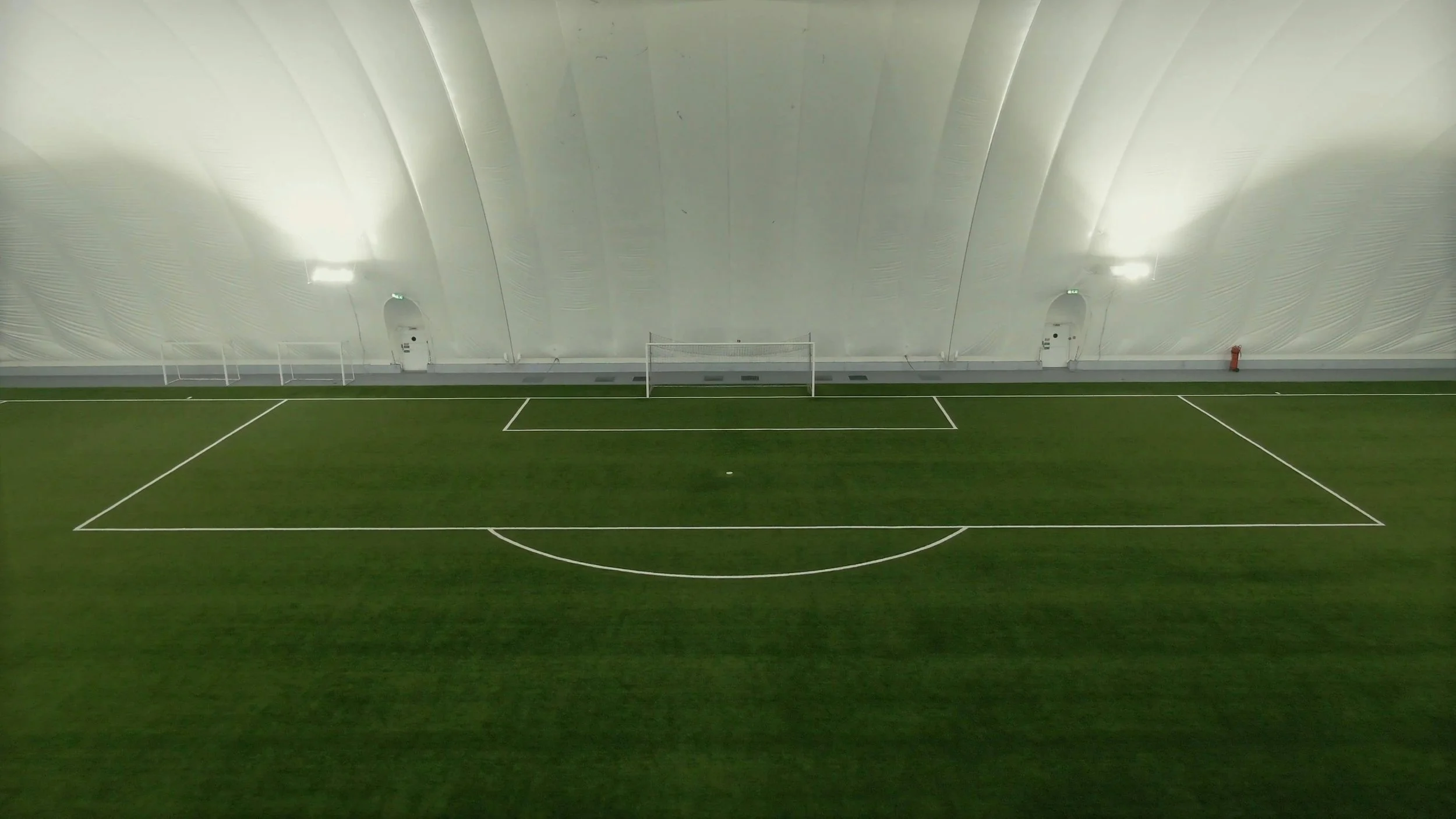 Indoor soccer field with green turf, white lines, goalposts, and a large white inflatable ceiling.