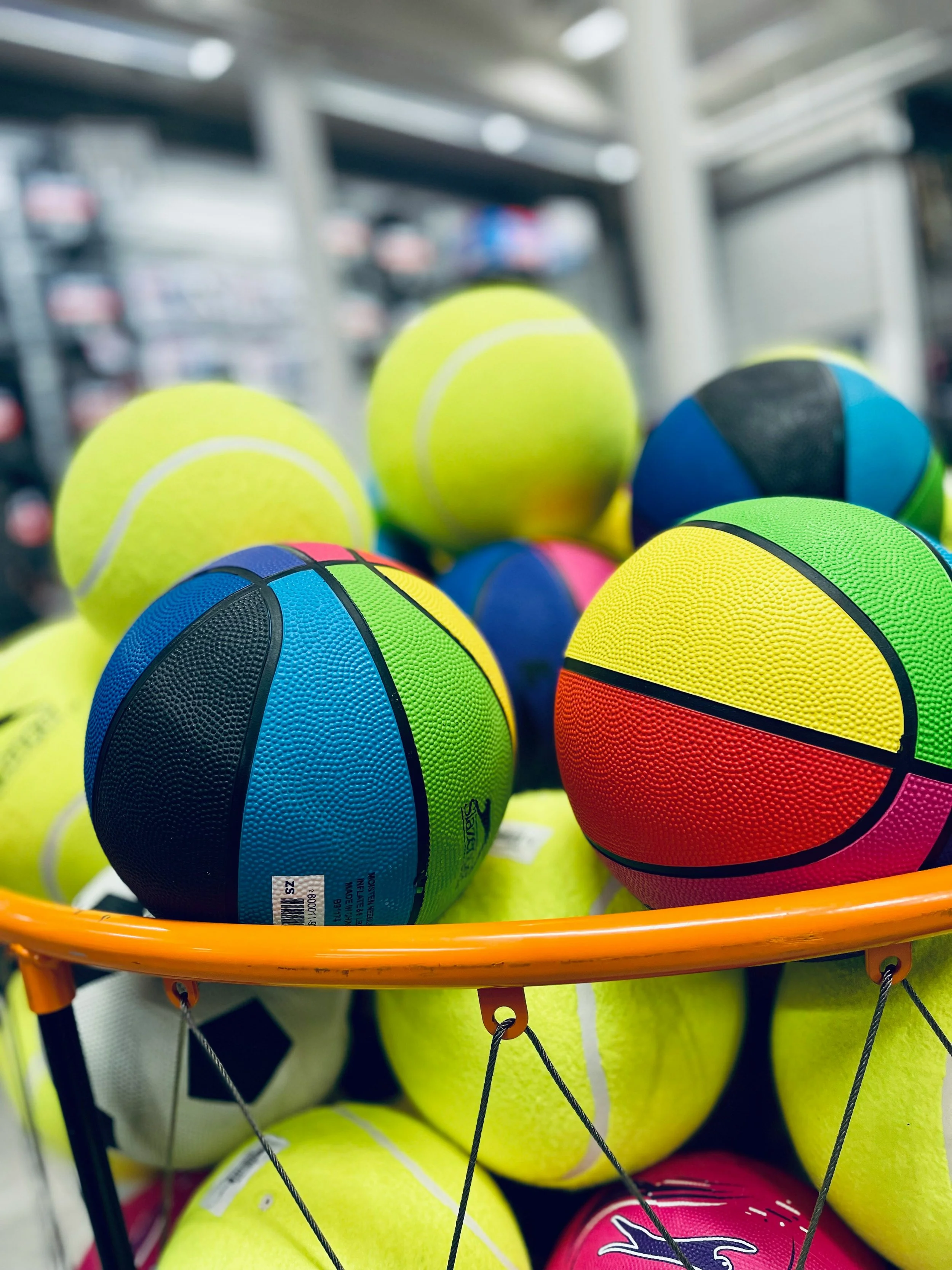 Colorful tennis balls in a shopping cart at a store.