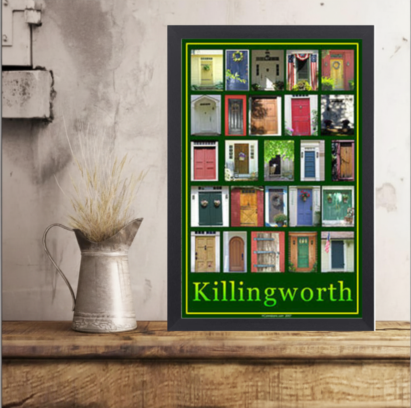 A poster with multiple images of various colorful doors and the word 'Killingworth' at the bottom in green text, placed next to a silver pitcher with dried plants on a wooden surface.
