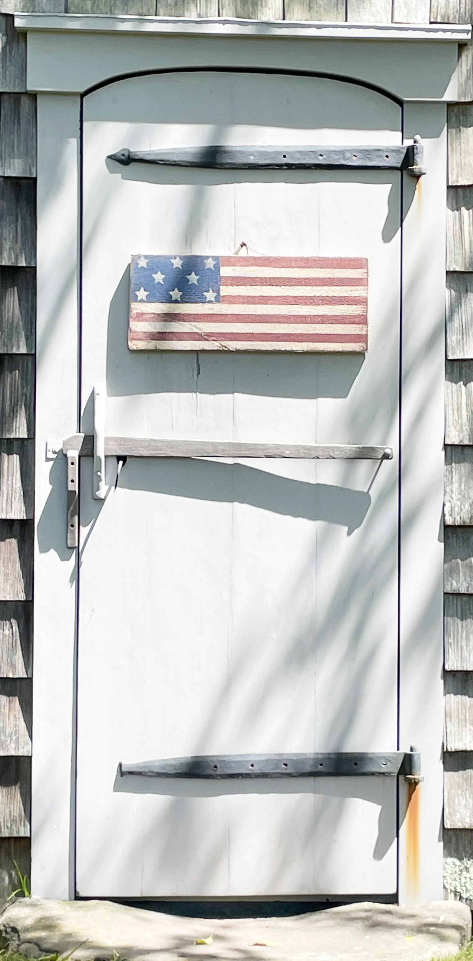 White door with a small American flag mounted on it, and three wooden shelves above and below the flag.