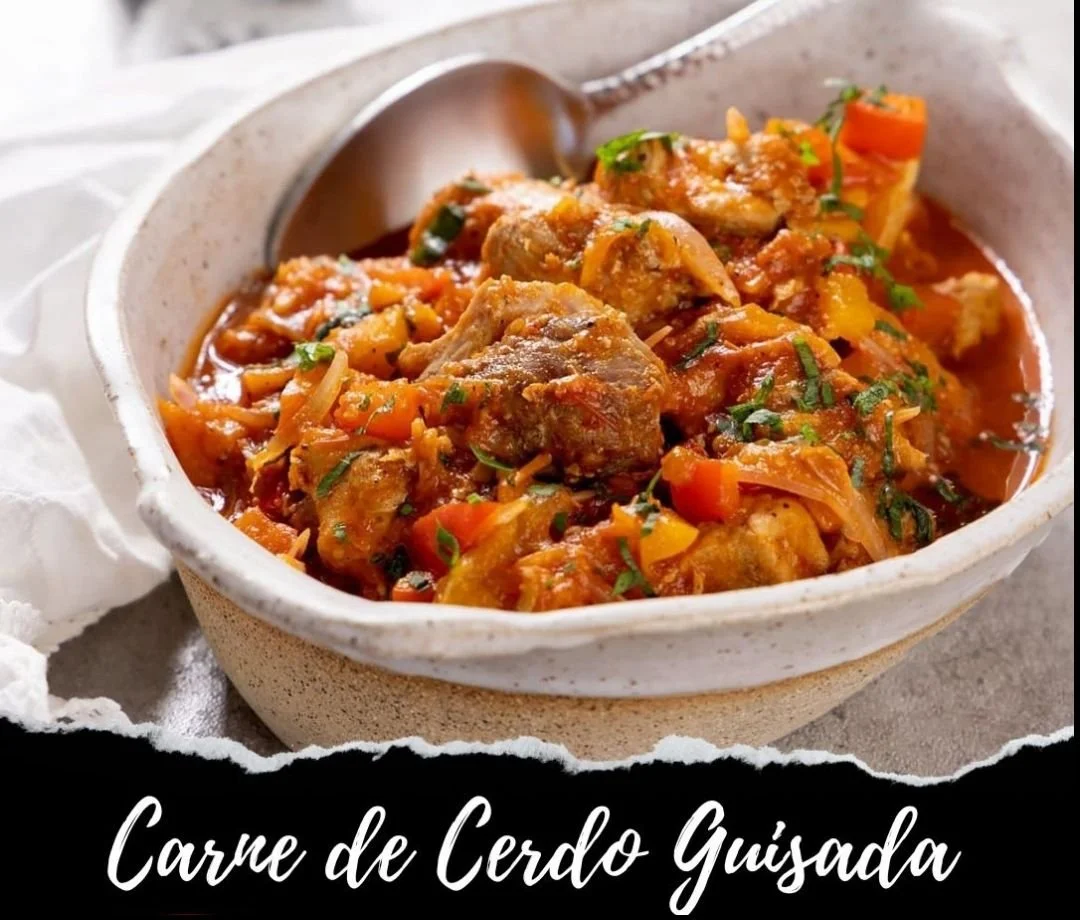 A bowl of Guisada pork stew with chunks of meat, vegetables, and herbs in a tomato-based sauce.