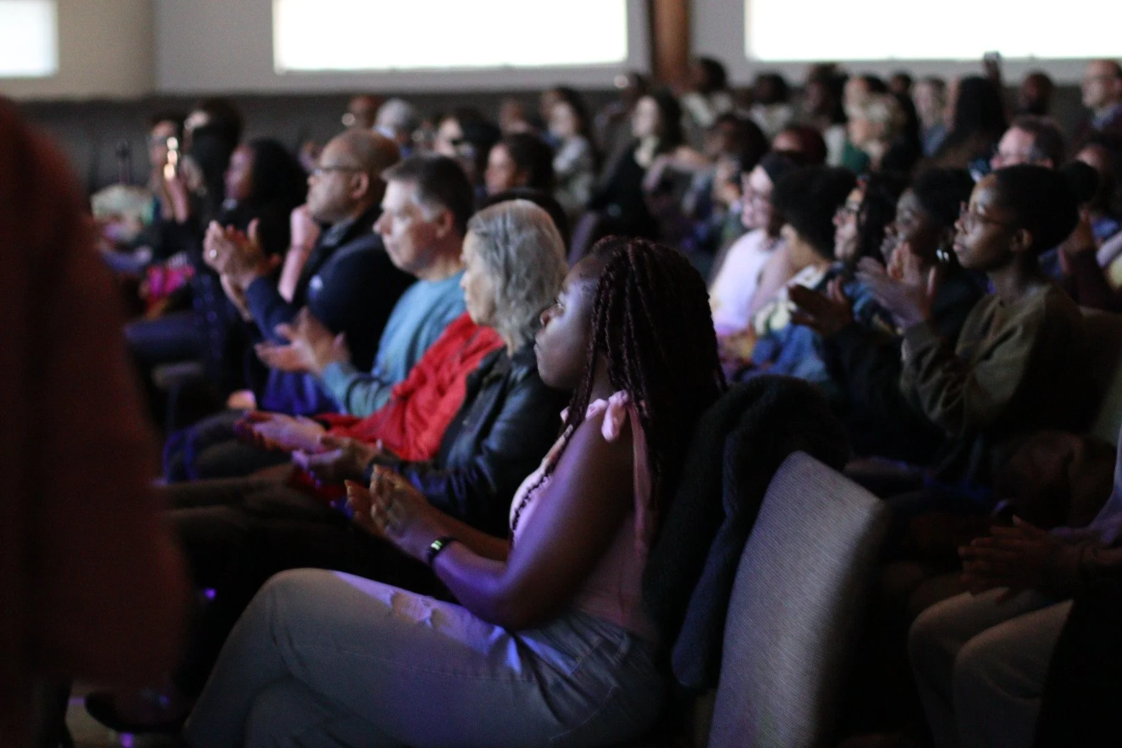 Audience seated in a dark auditorium, attending a presentation or event, with their attention focused on the stage or screen.
