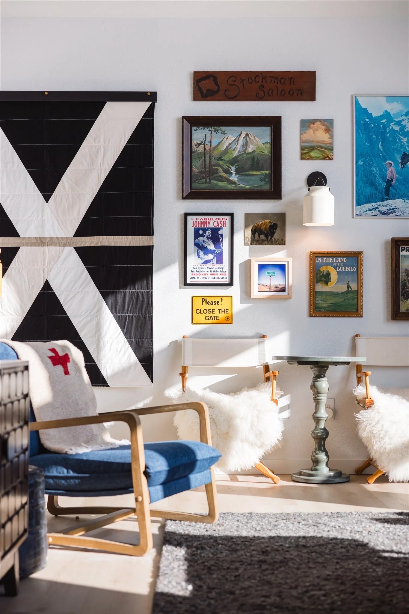 Interior of a cozy room with a gallery wall, blue midcentury chair with wooden arms, and a round table. Wall art includes mountain and landscape paintings, and a Johnny Cash poster.