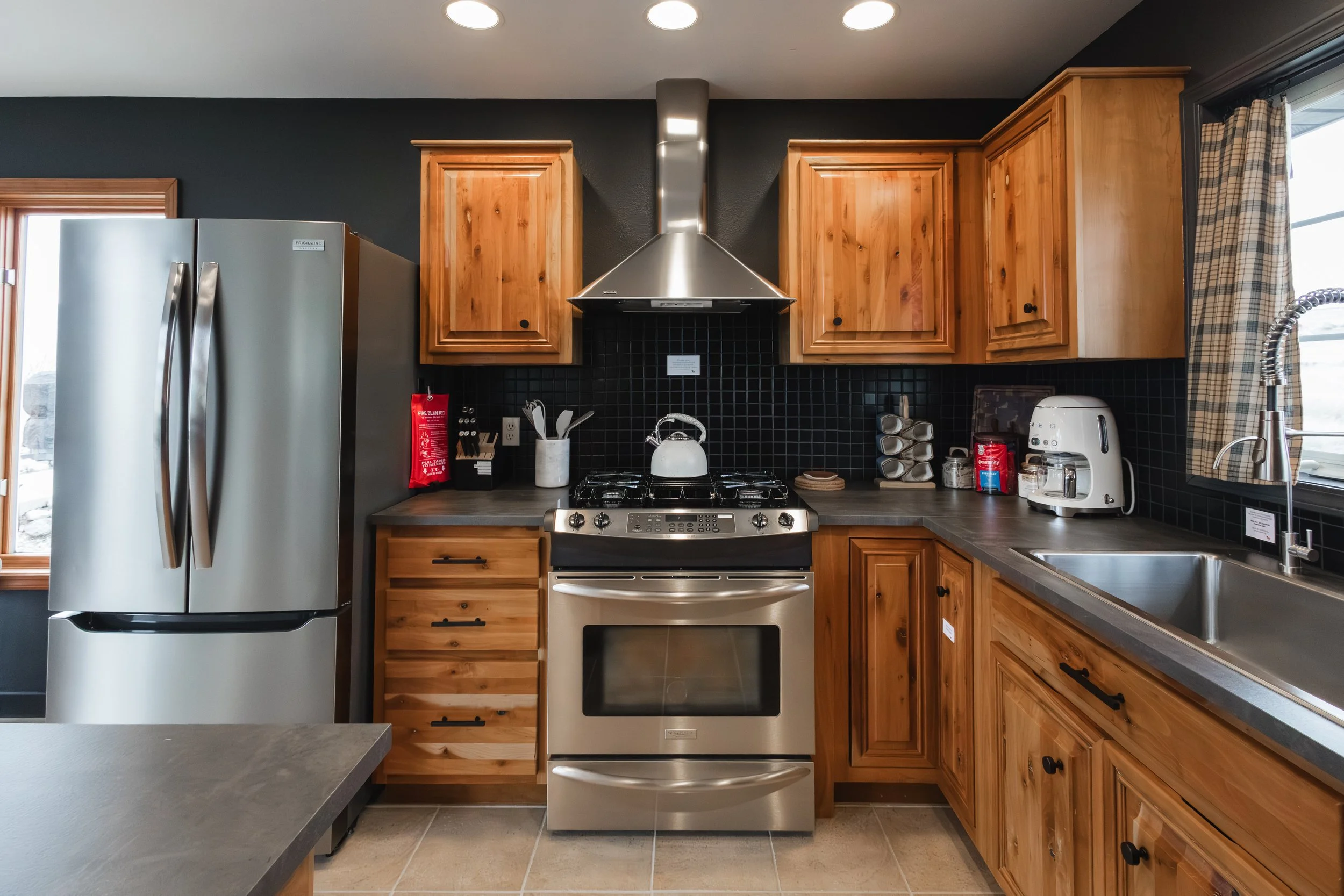 Kitchen with wooden cabinets, stainless steel stove with pots, black tile backsplash, a side-by-side refrigerator, a white toaster, and a kitchen sink.