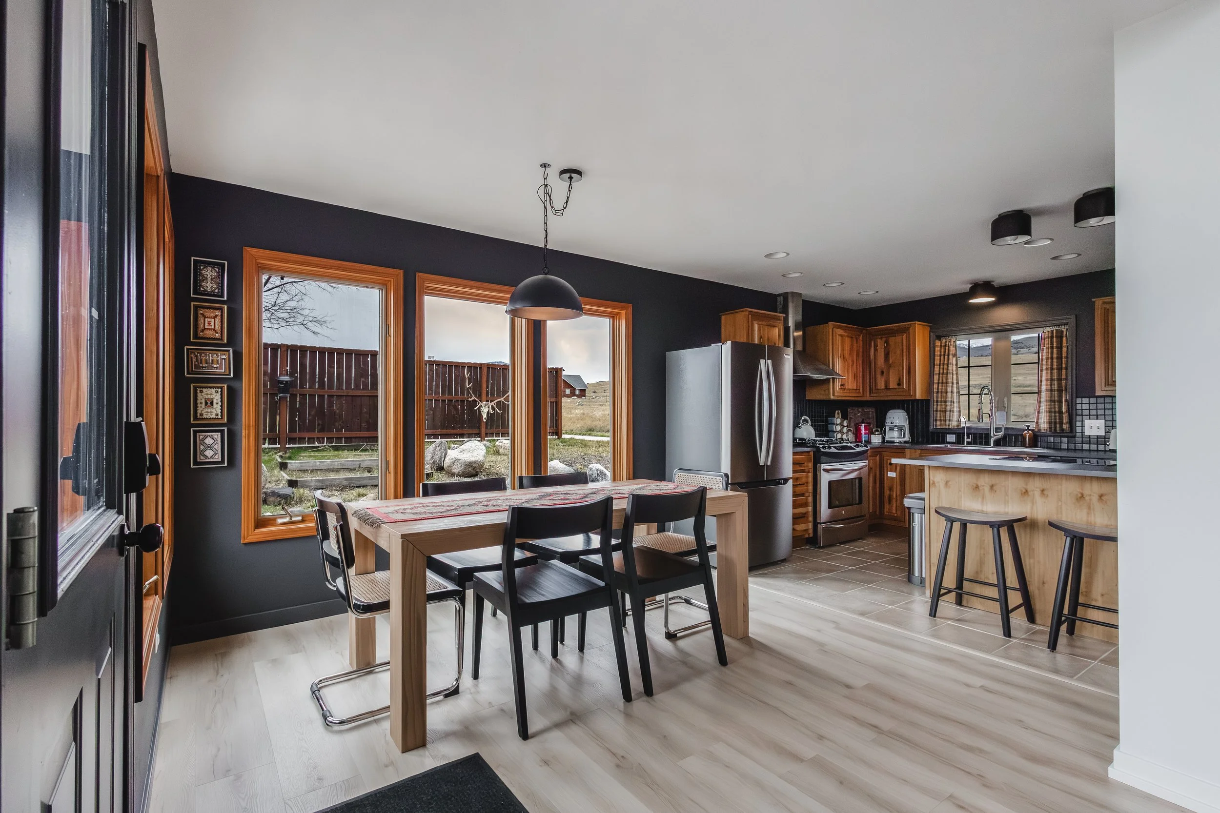 Kitchen with wooden cabinets, stainless steel refrigerator, window overlooking a backyard, dining table with chairs, and a view of the living area