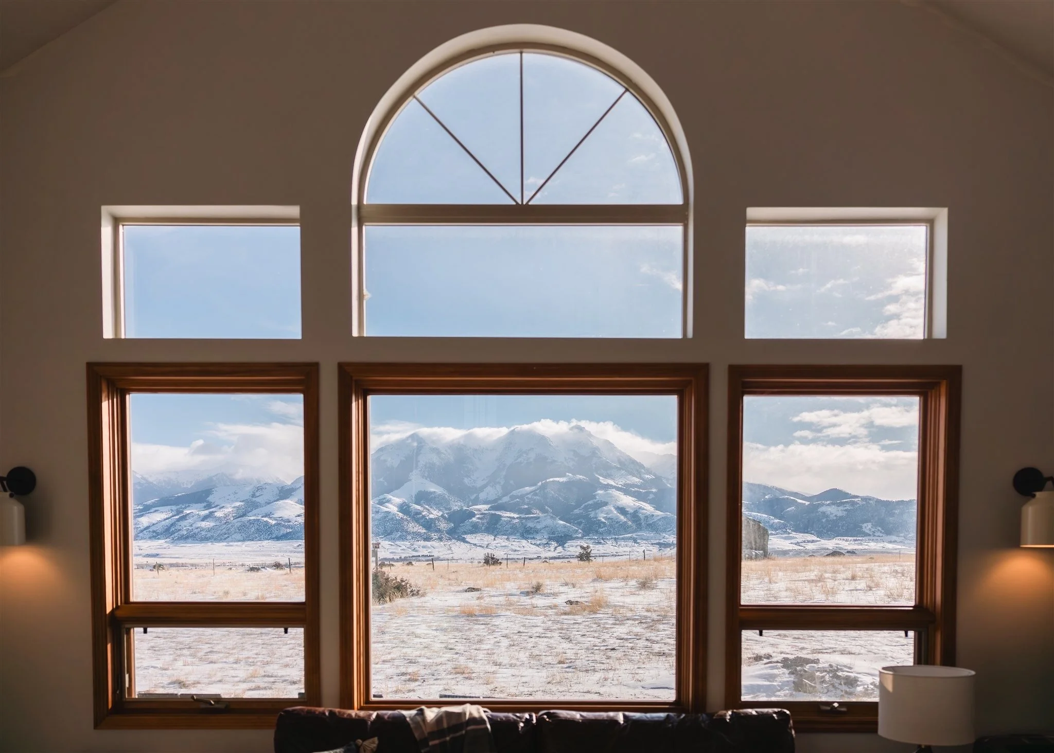 Room with large arched and rectangular windows overlooking a snow-covered landscape with Absaroka mountains in the distance.