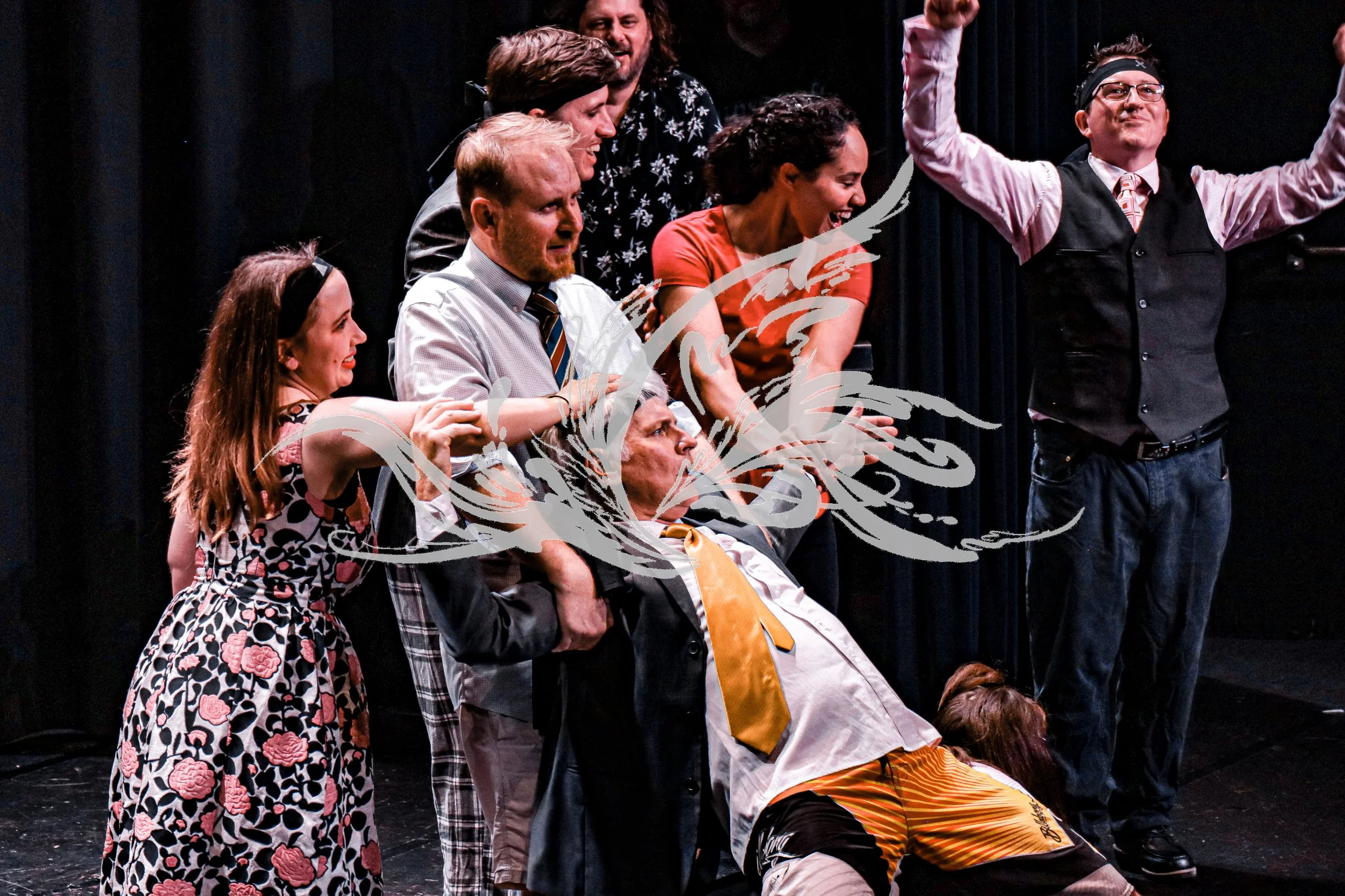 Group of six diverse people on stage, some sitting and some standing, laughing and celebrating, with dark curtains in the background.