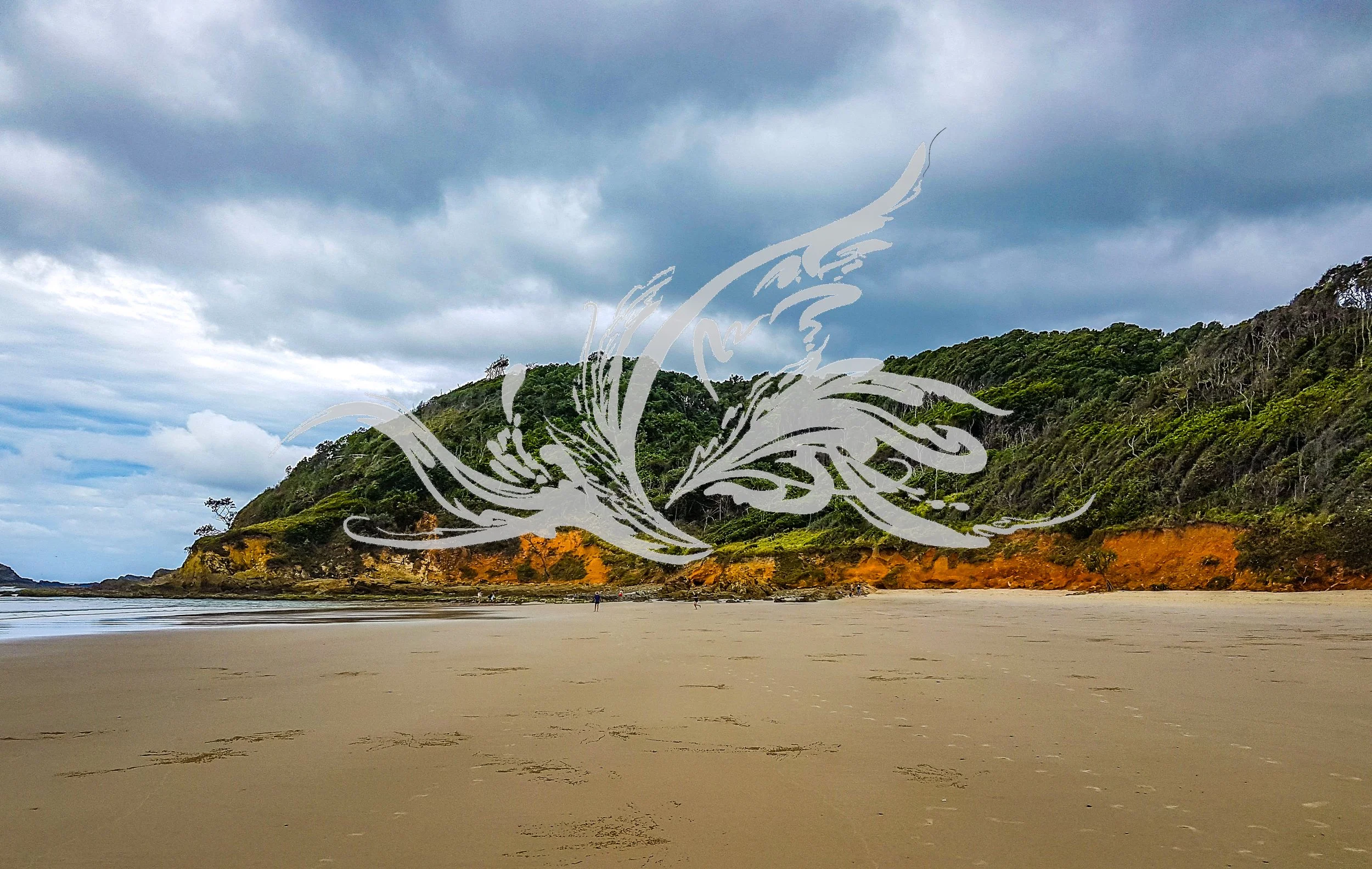 A beach with sand, a few people, green hills with trees, cliffs, and a cloudy sky.