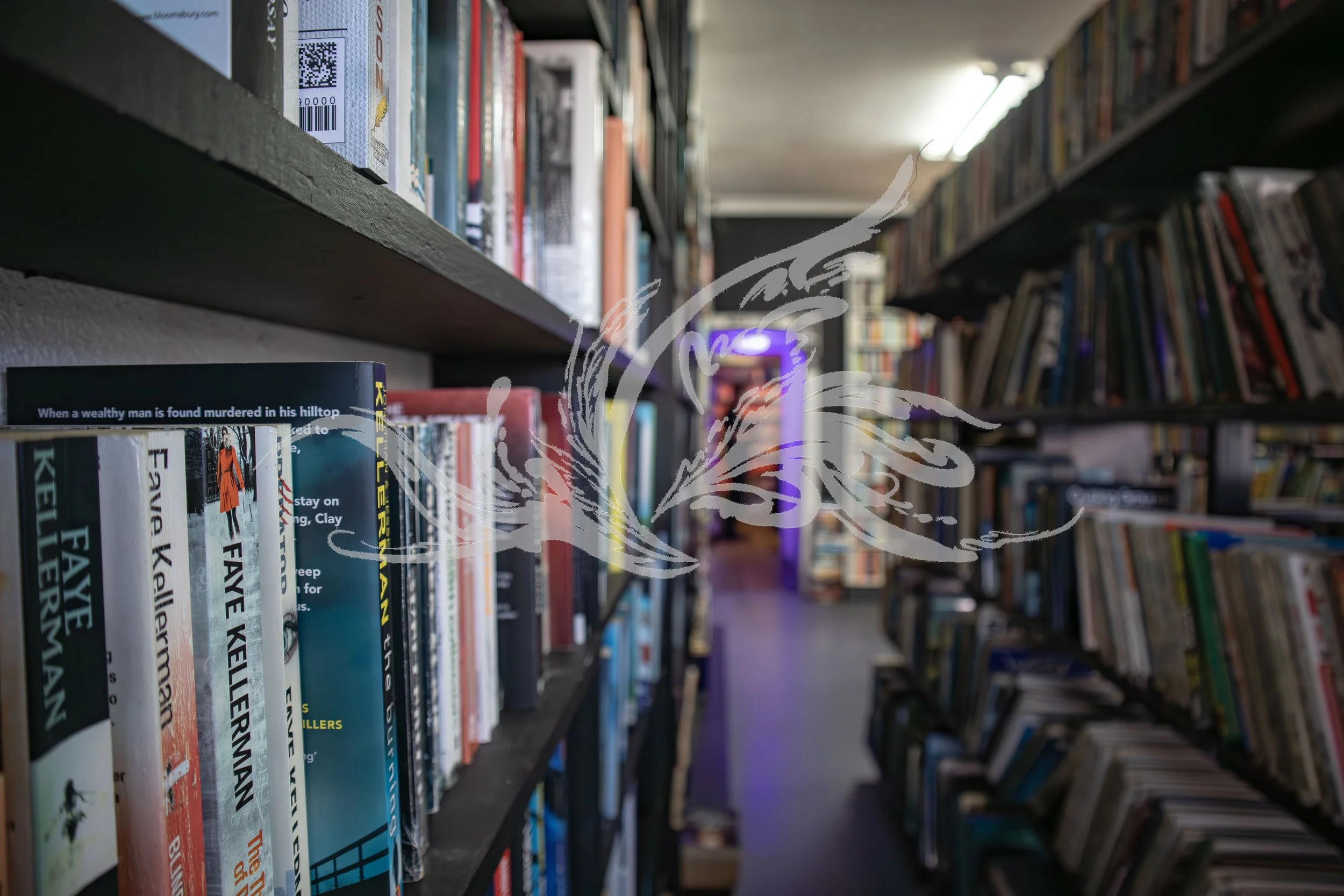 A wide aisle in a bookstore or library with shelves full of books on both sides. The books on the left are arranged vertically with words visible on their spines, and the shelves extend into the distance, creating a sense of depth.