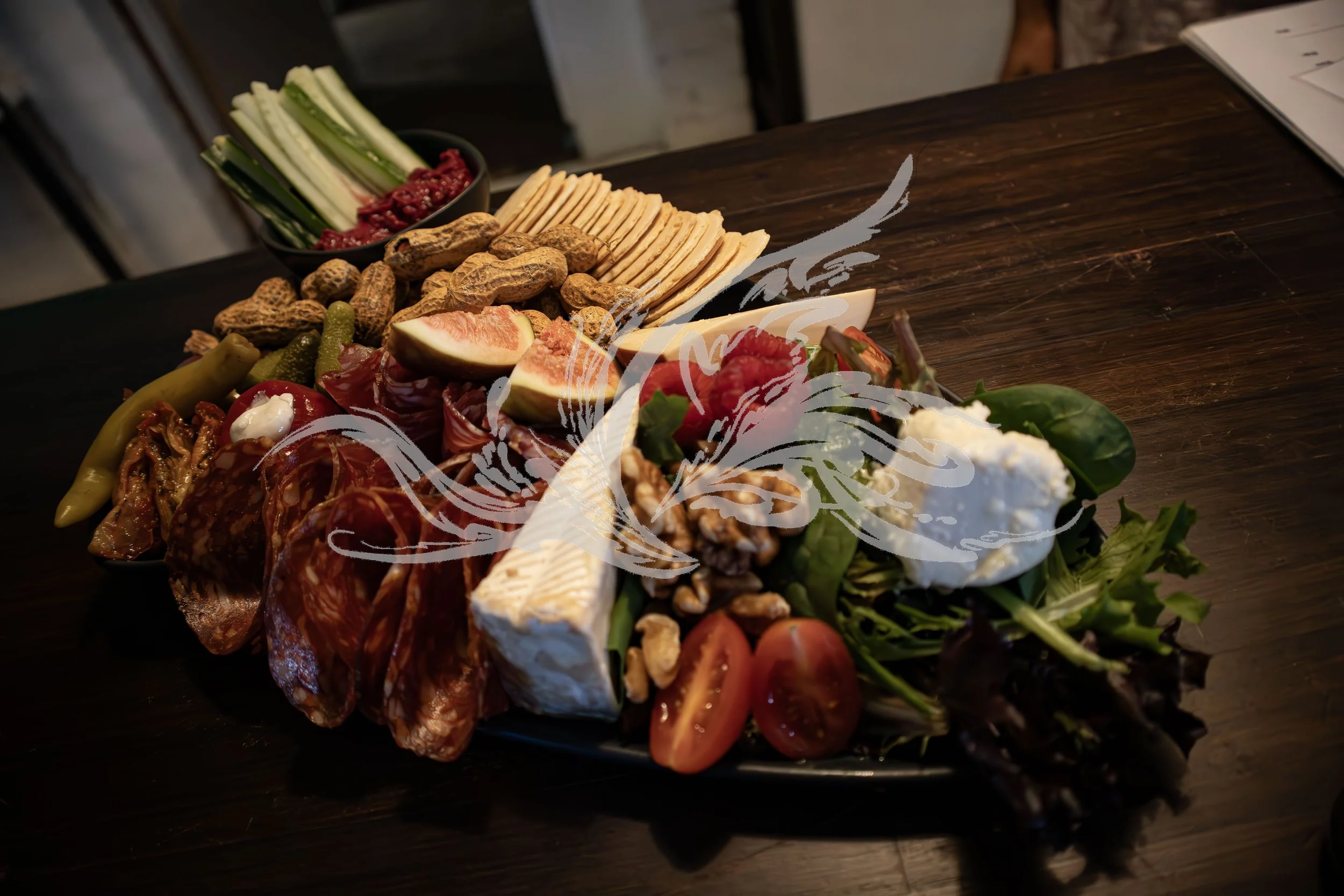 A large platter of assorted cheeses, nuts, fresh vegetables, figs, cured meats, and crackers on a dark wooden table.