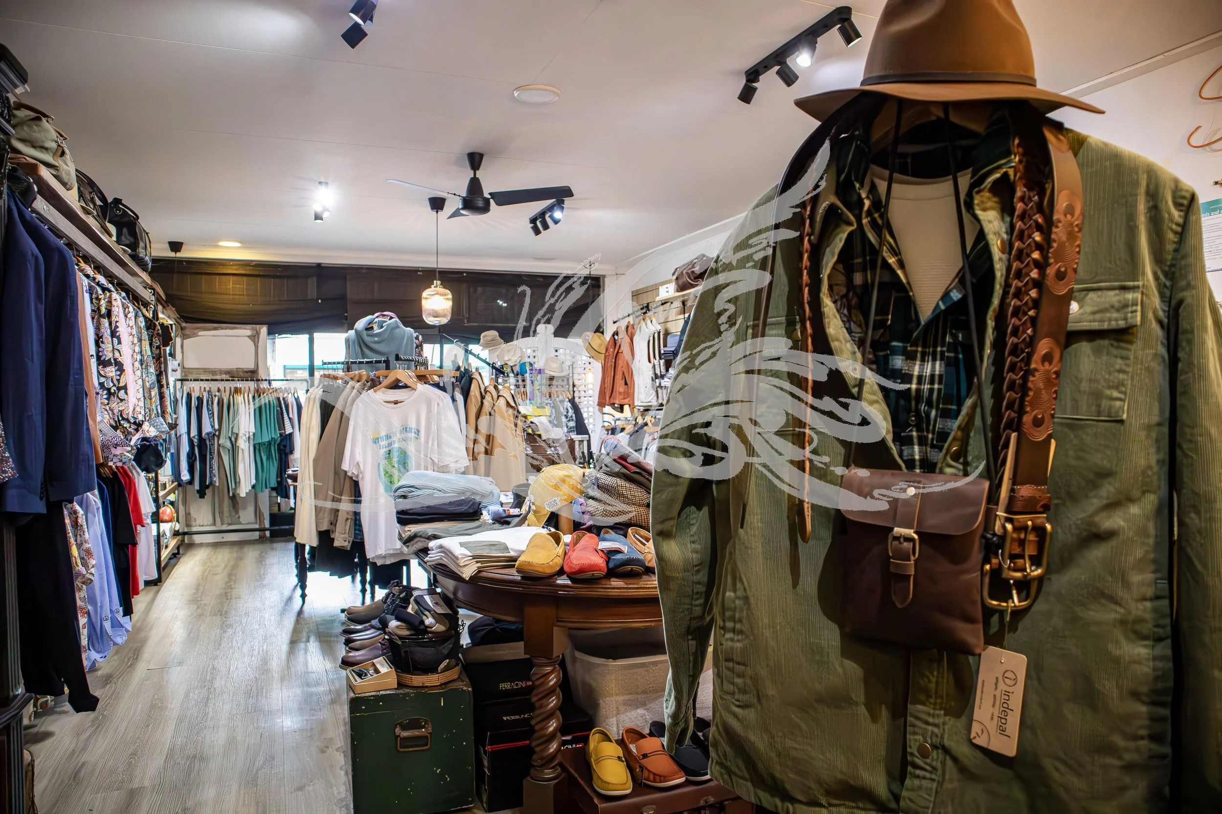 Clothing store interior with racks of assorted clothes, hats, and shoes on display, featuring a mannequin dressed in a green jacket, plaid shirt, and wide-brimmed hat.