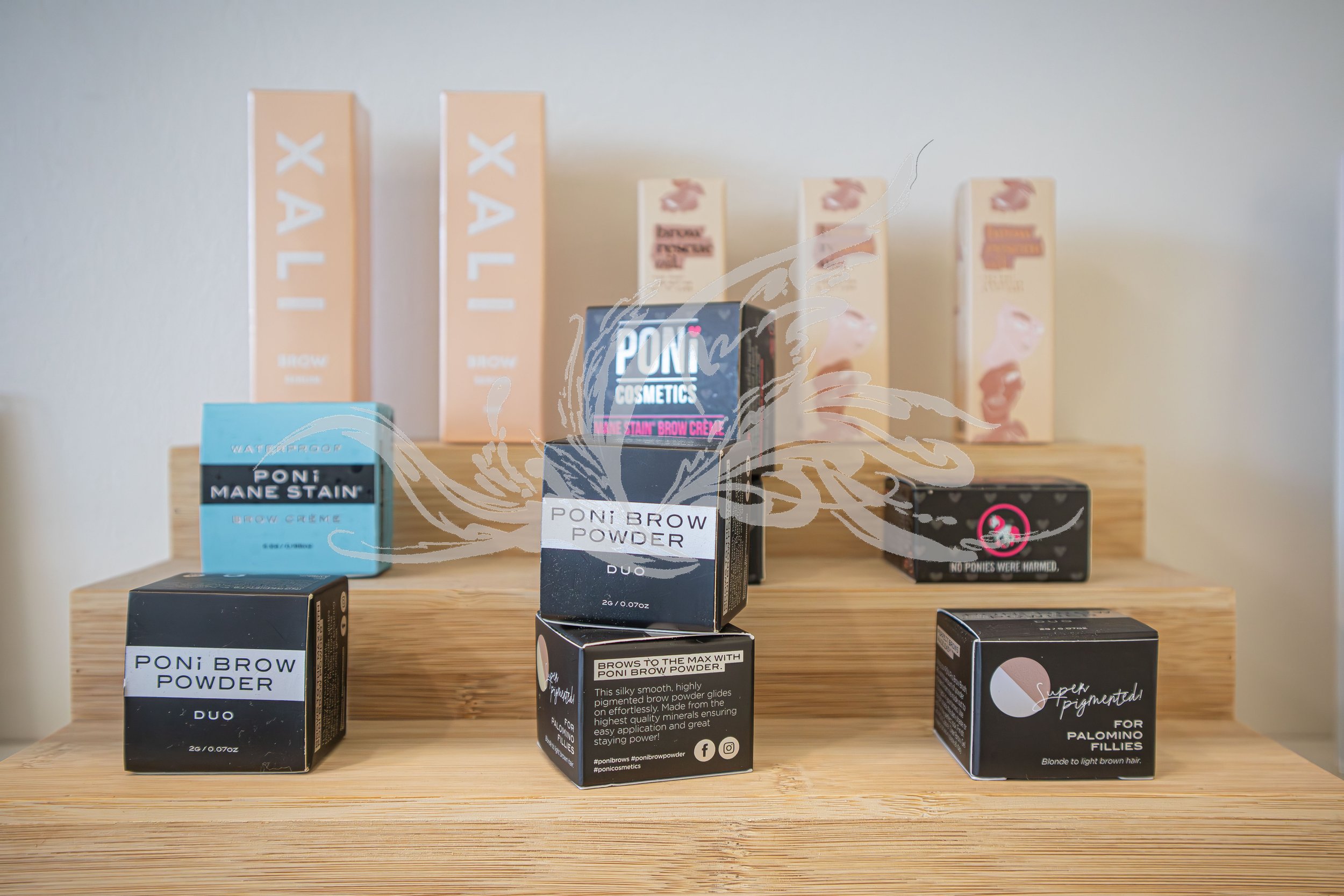 Display of cosmetic products on a wooden shelf, including Poni Brow Powder in various shades, with packaging labels and branding visible, and a sign mentioning the product as super pigmented.