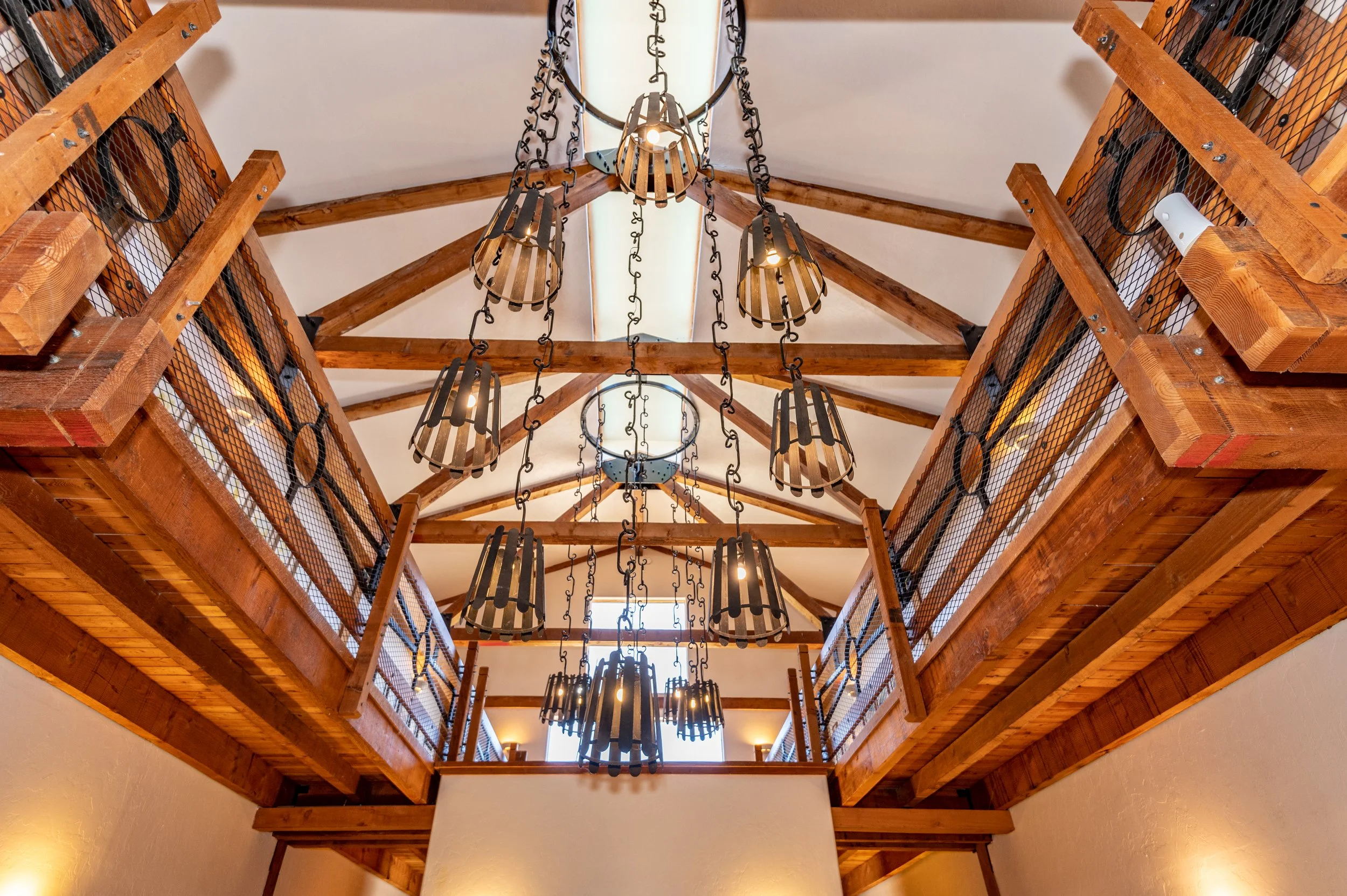 A ceiling with wooden beams and a central skylight, decorated with hanging pendant lights with black metal frames in a rustic style.