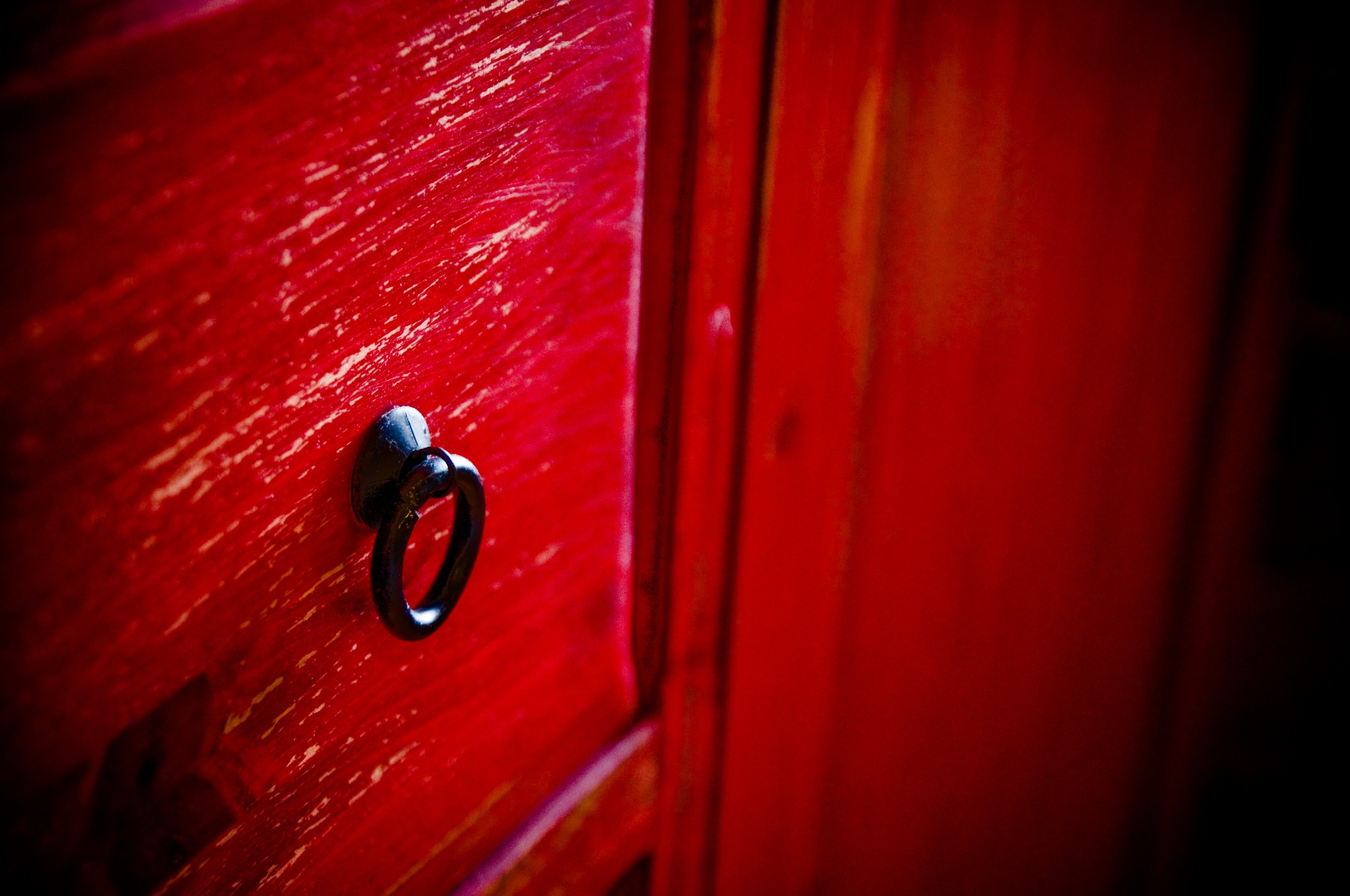 Close-up of a red-painted wooden door with a metallic door handle and a ring key in it.