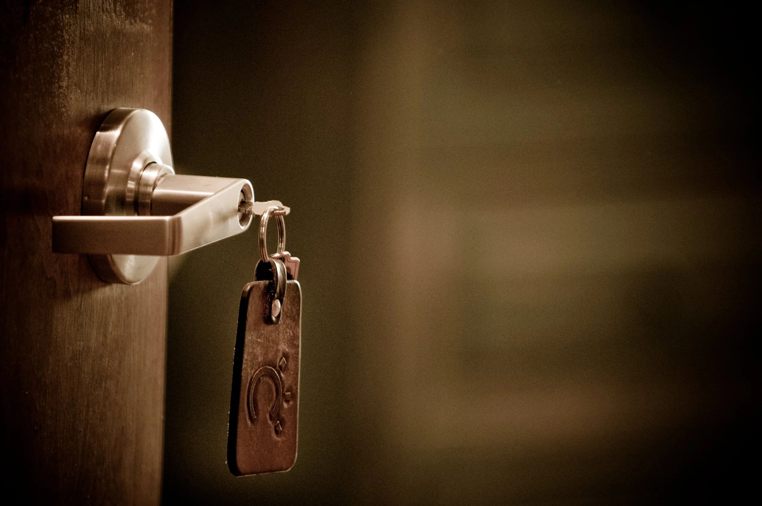 A close-up of a door lock with keys hanging from it, mounted on a wooden door.