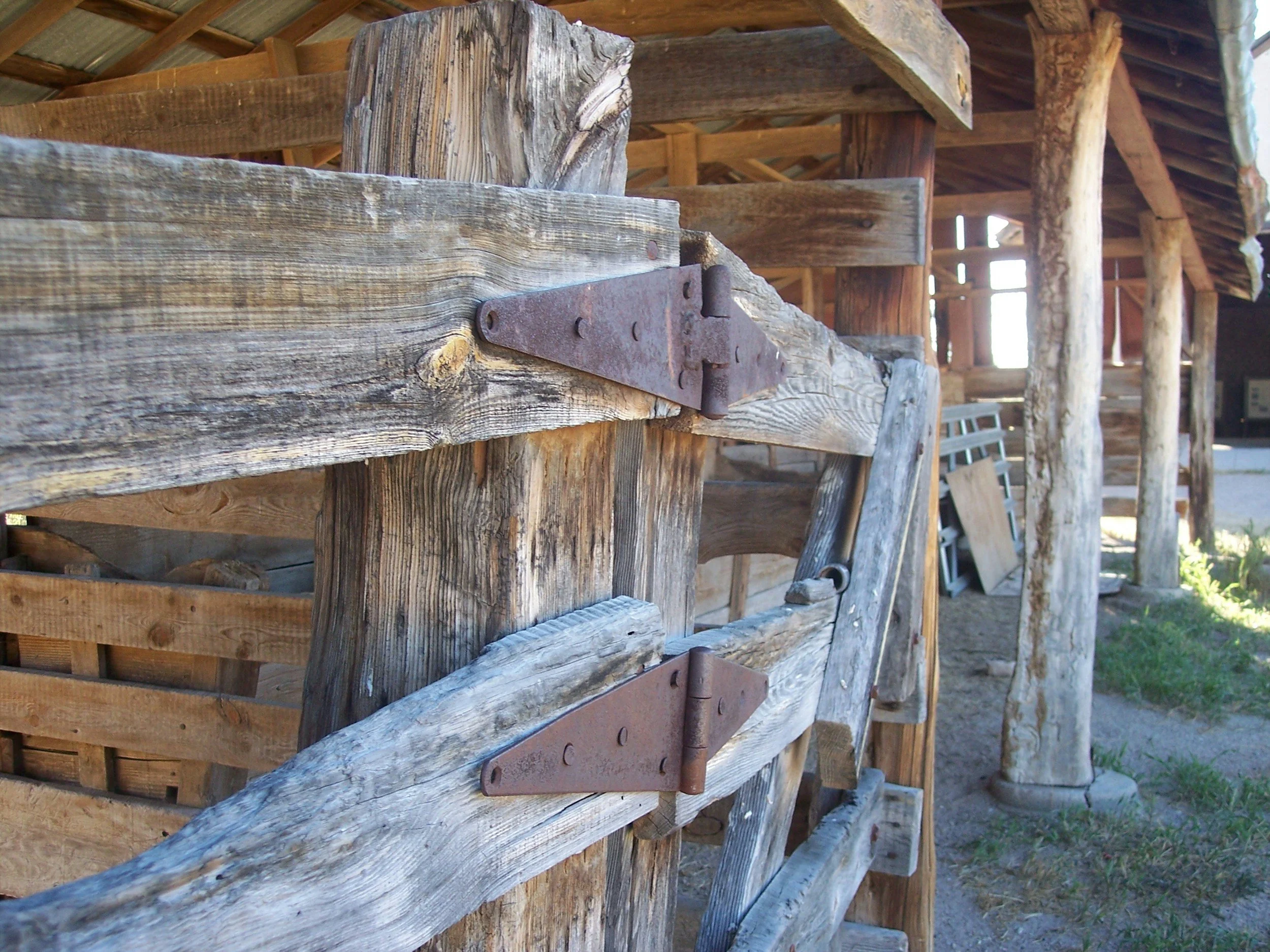 Close-up of a weathered wooden structure with rusted metal hinges and bolts, featuring rough, aged wood and support beams, set in an outdoor rustic setting.
