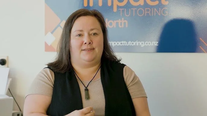 A woman with shoulder-length brown hair wearing a beige shirt and black vest, standing in front of a wall with the ImpacTutor logo and website.