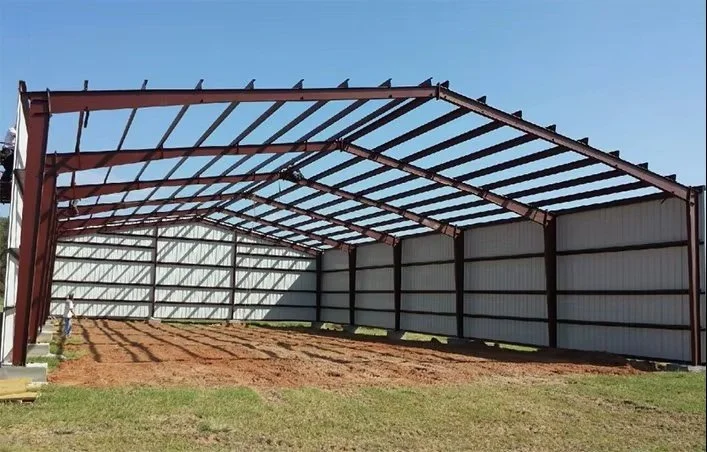 Metal building frame with a curved roof under construction in an open grassy area.