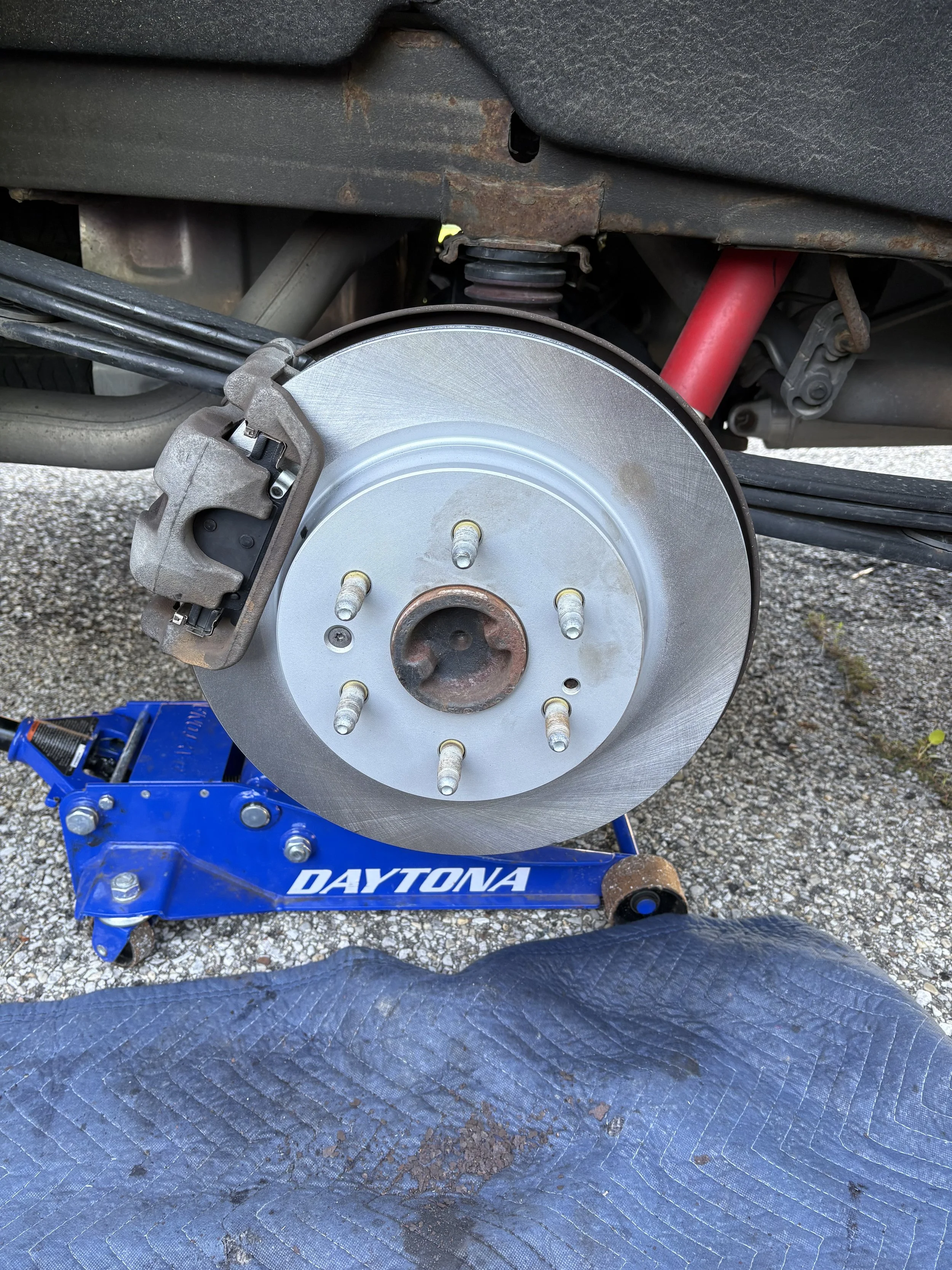 Close-up of a car's brake rotor and caliper mounted on a blue stand. New breaks for this customers car.