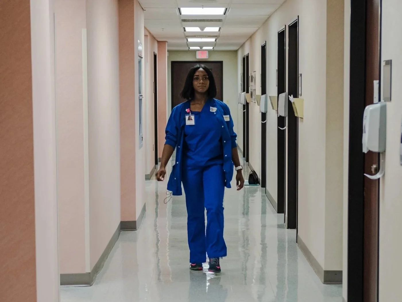 A YouthForce NOLA intern walks down a medical office hallway in blue scrubs.