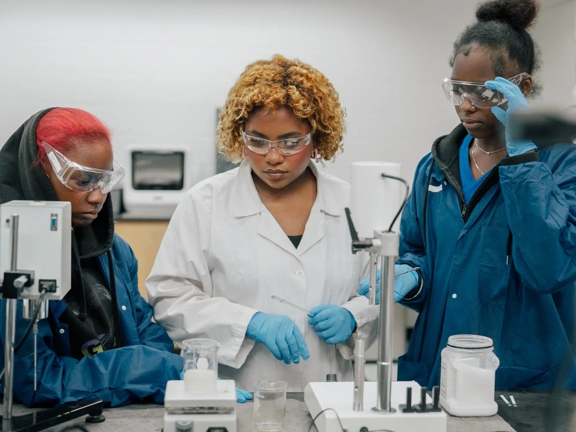 Three black women stand behind several pieces of science equipment 
